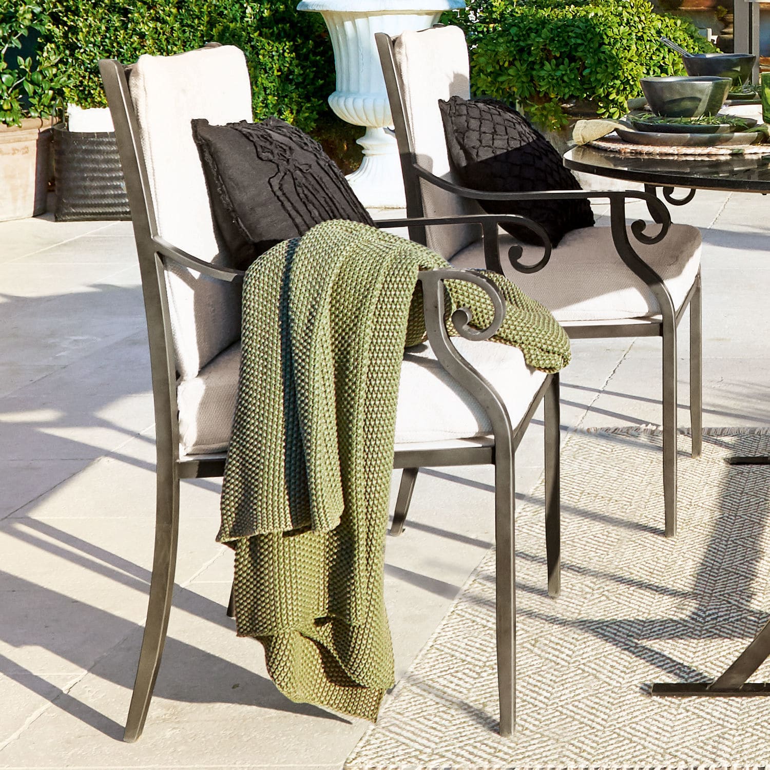 Sedie da giardino in metallo con cuscini crema e coperta verde lavorata a maglia su terrazza in pietra chiara