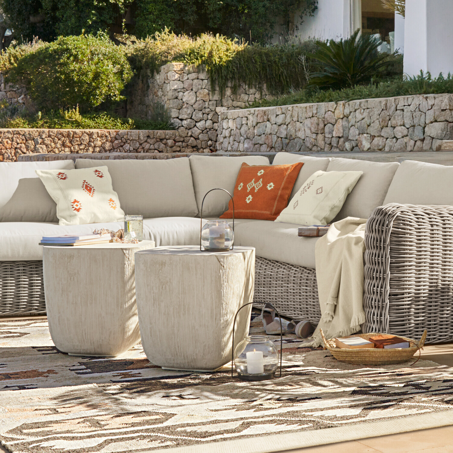 Set di mobili da esterno con divano in rattan beige e due tavolini chiari su terrazza
