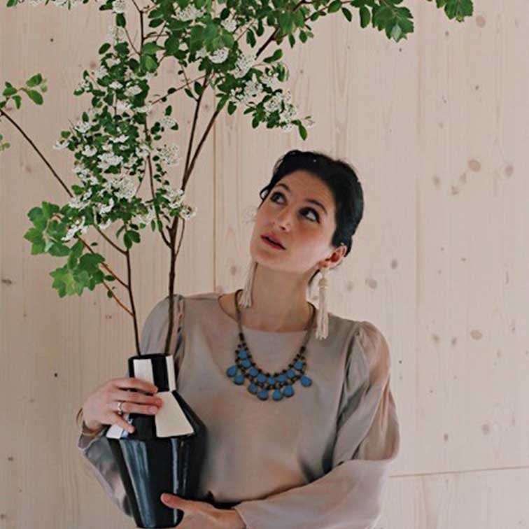 Donna con vaso in ceramica bianco e nero con rami verdi davanti a parete in legno chiaro