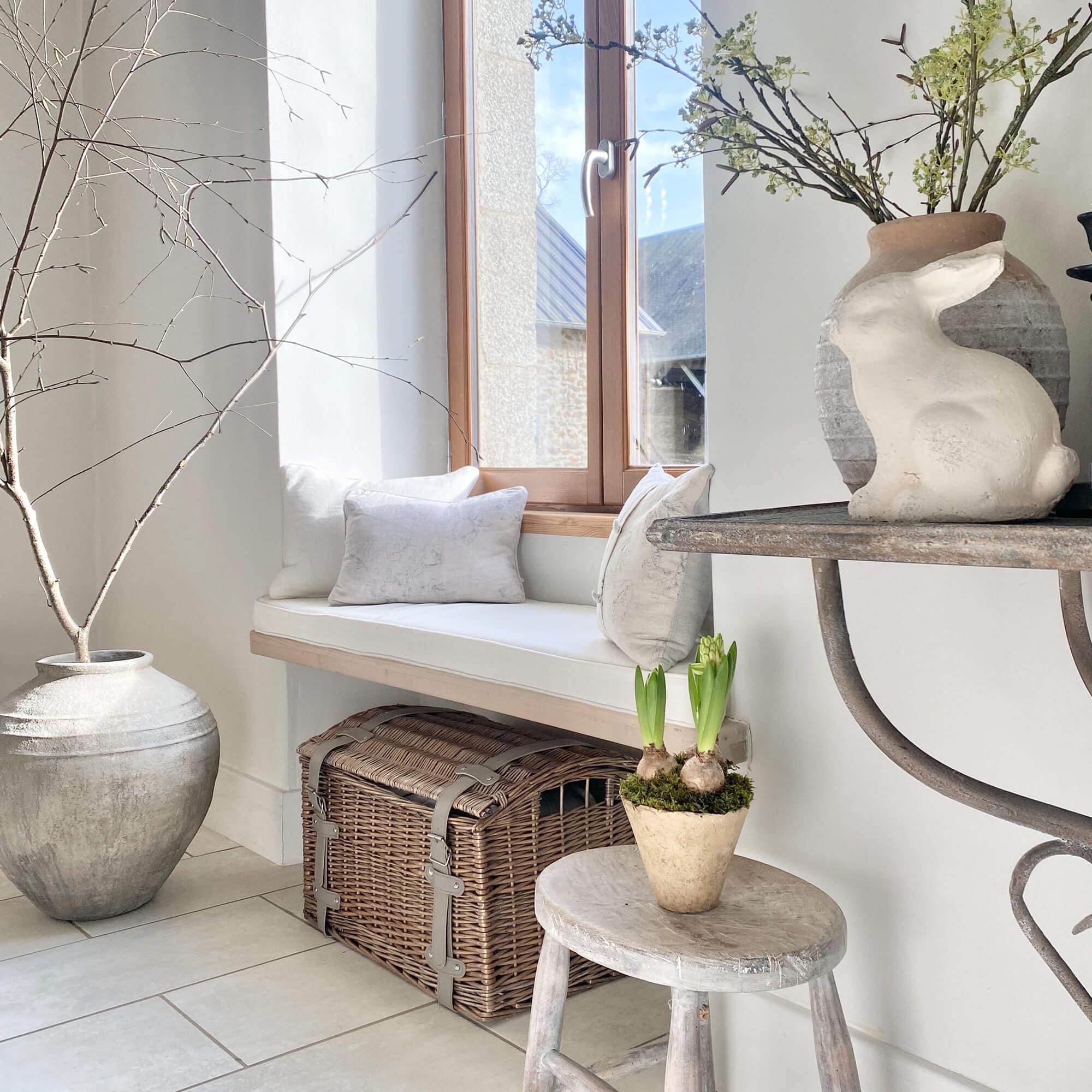 Angolo accogliente con cuscini bianchi, cassa in vimini e decorazione con coniglio in interno luminoso