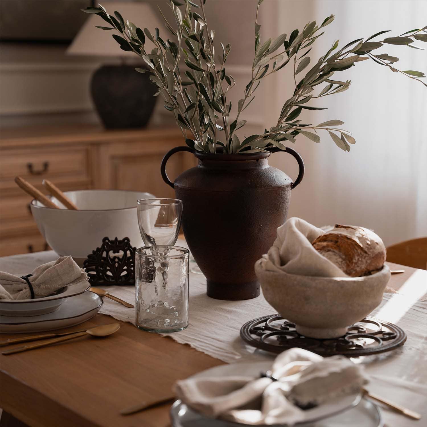 Vaso rustico in ceramica marrone con rami verdi su tavolo in legno con stoviglie