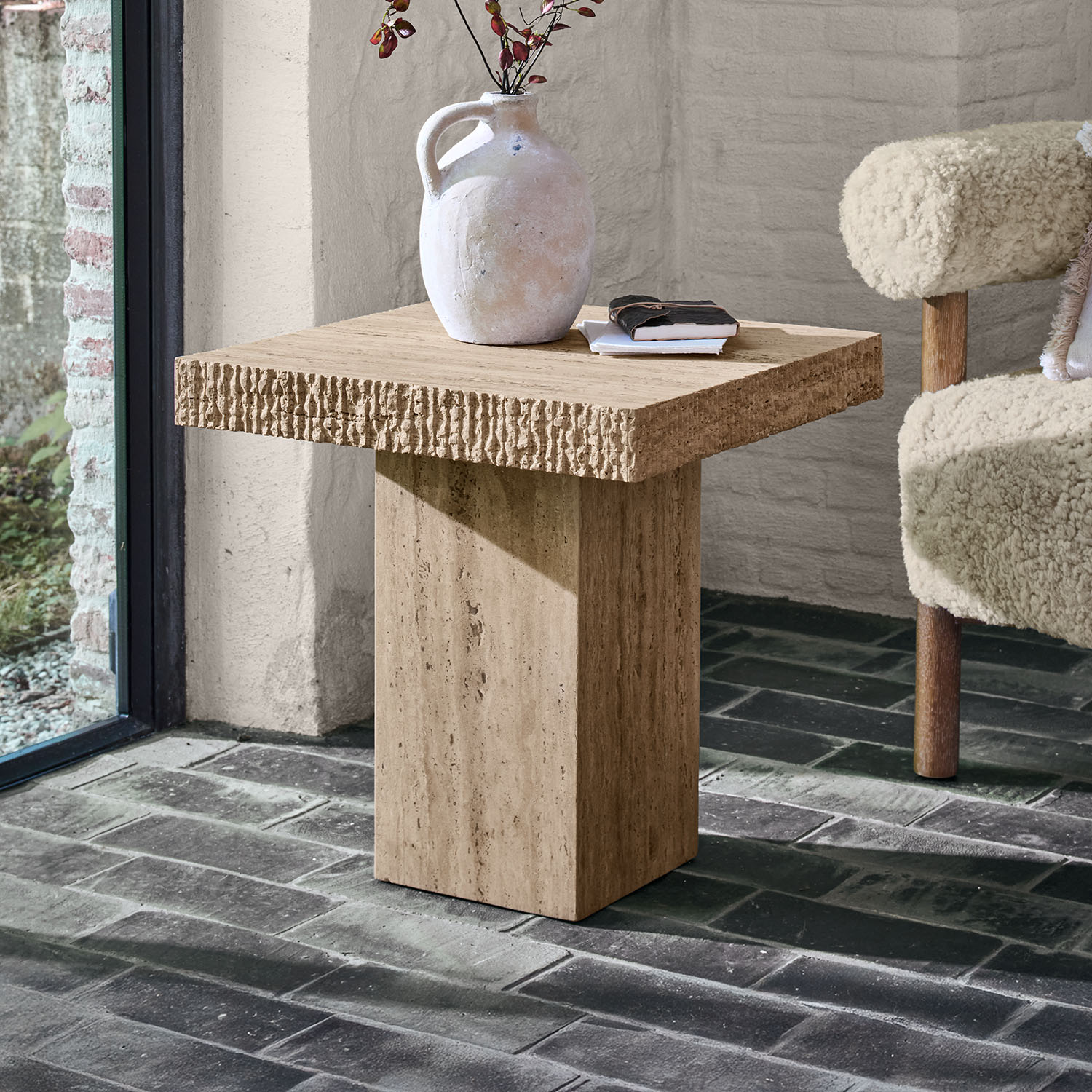 Tavolino quadrato in travertino beige con brocca decorativa e libri sopra