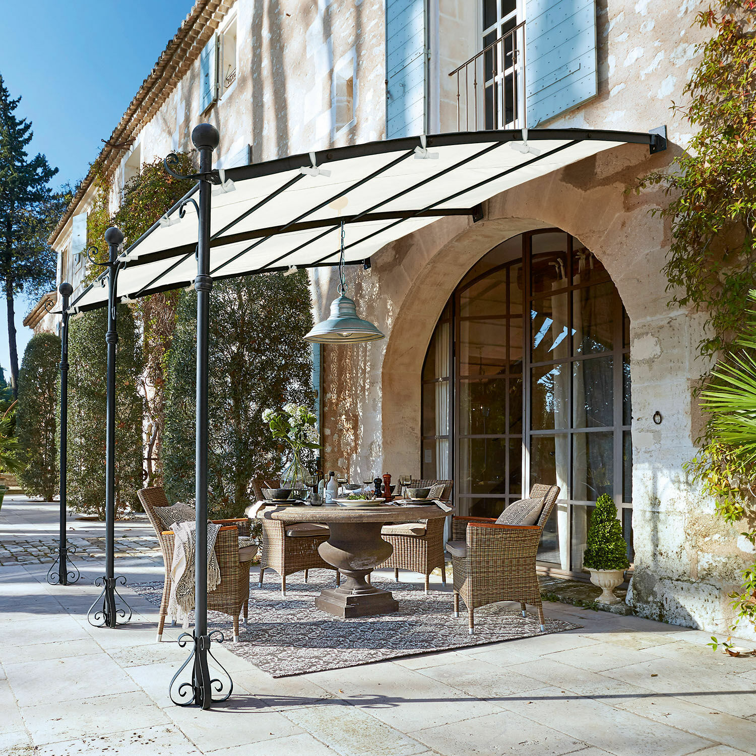 Pergola Kattles Set di mobili da giardino in rattan sotto una tettoia bianca su un patio in pietra davanti a una casa in pietra