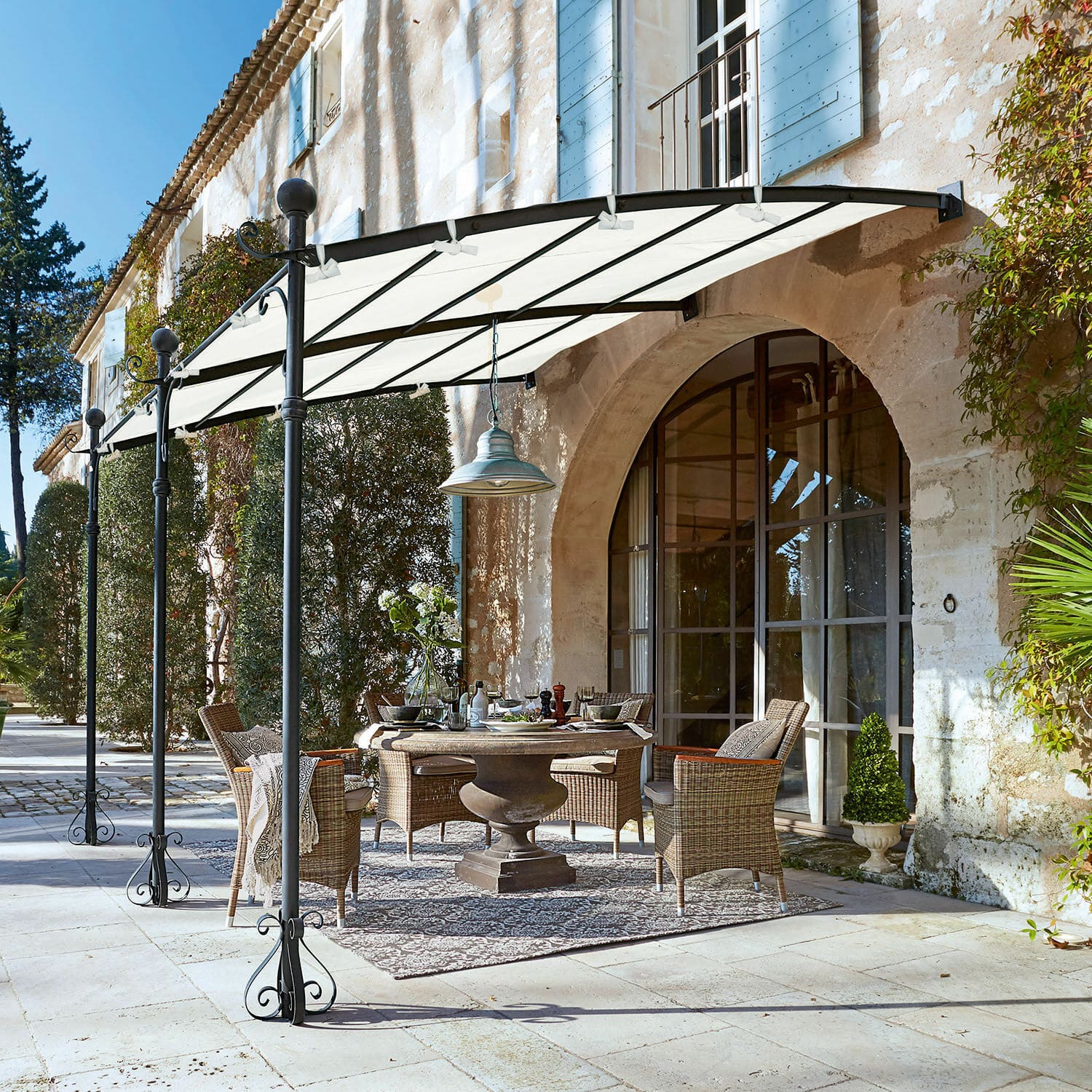 Pergola Kattles Set di mobili da giardino in rattan sotto una tettoia bianca su un patio in pietra davanti a una casa in pietra