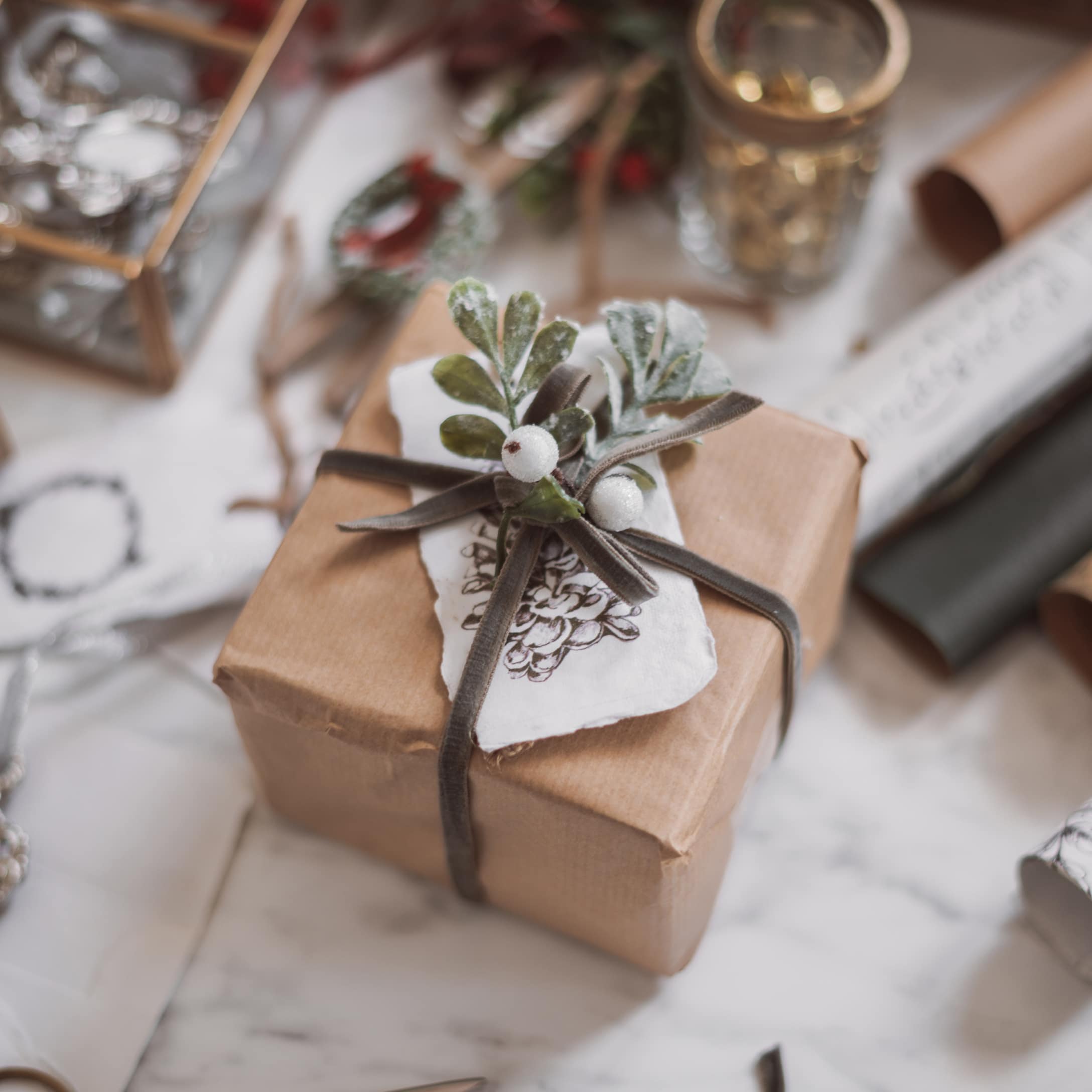 Regalo avvolto in carta marrone con nastro grigio e foglie verdi per decorazione natalizia