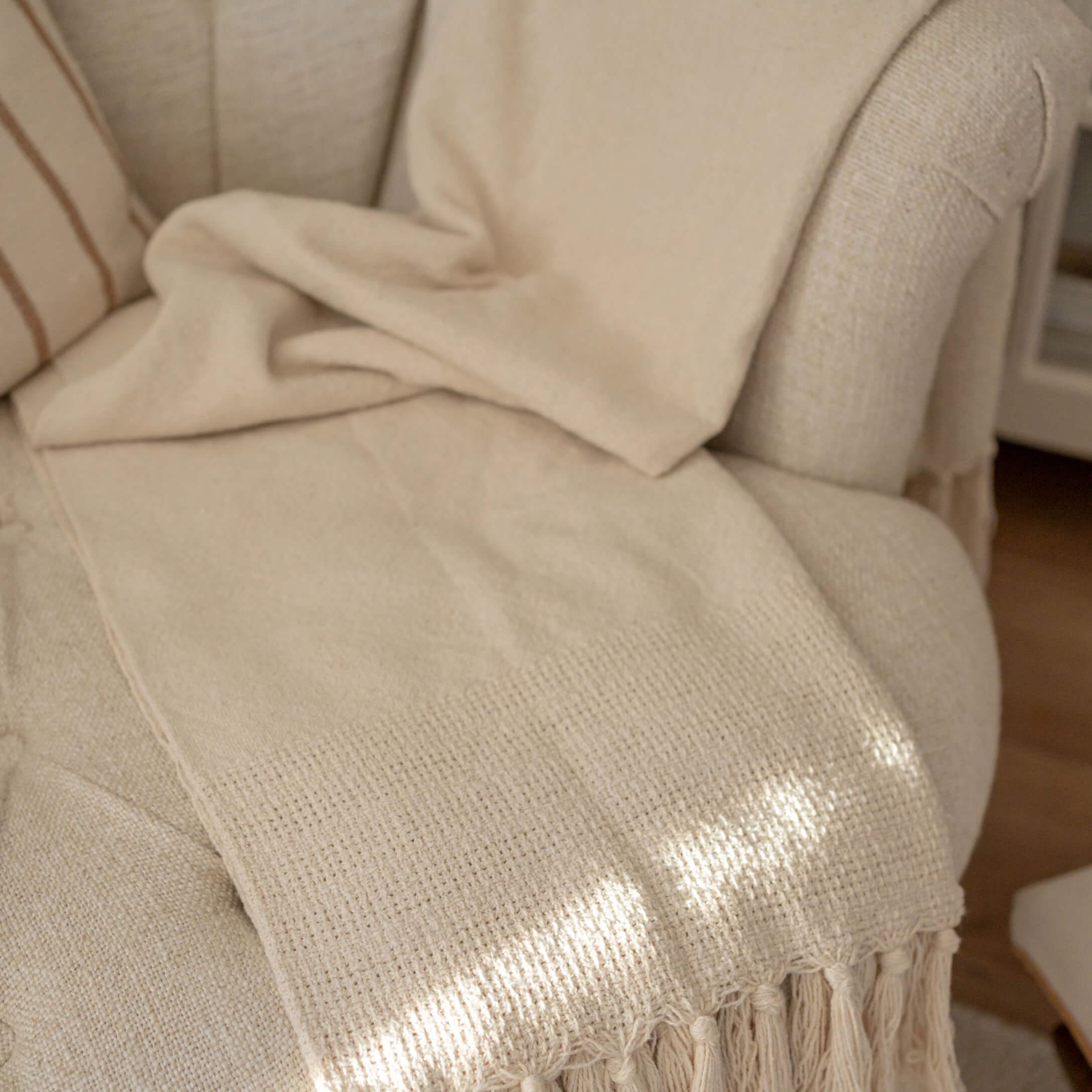 Coperta beige con frange su poltrona chiara, tessuto morbido per decorazione e comfort