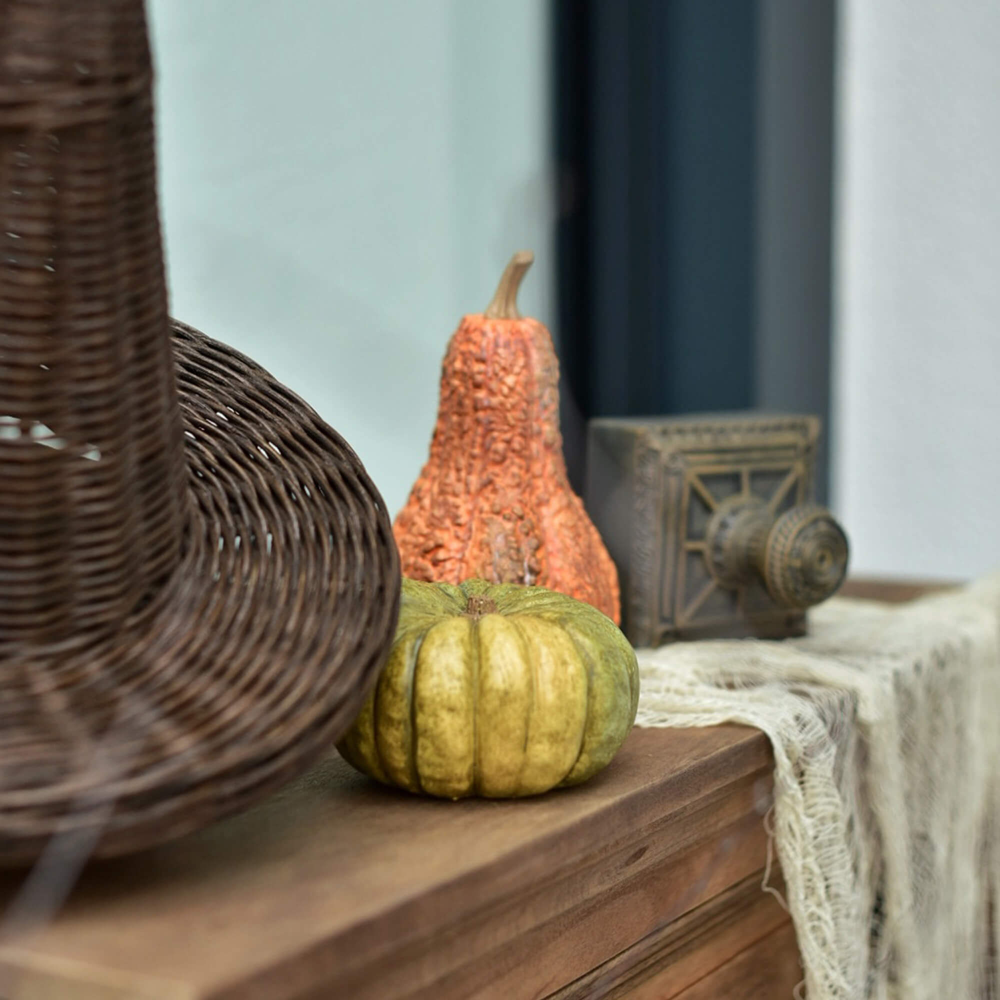 Zucca decorativa verde e arancione su piano in legno accanto a un cesto di vimini