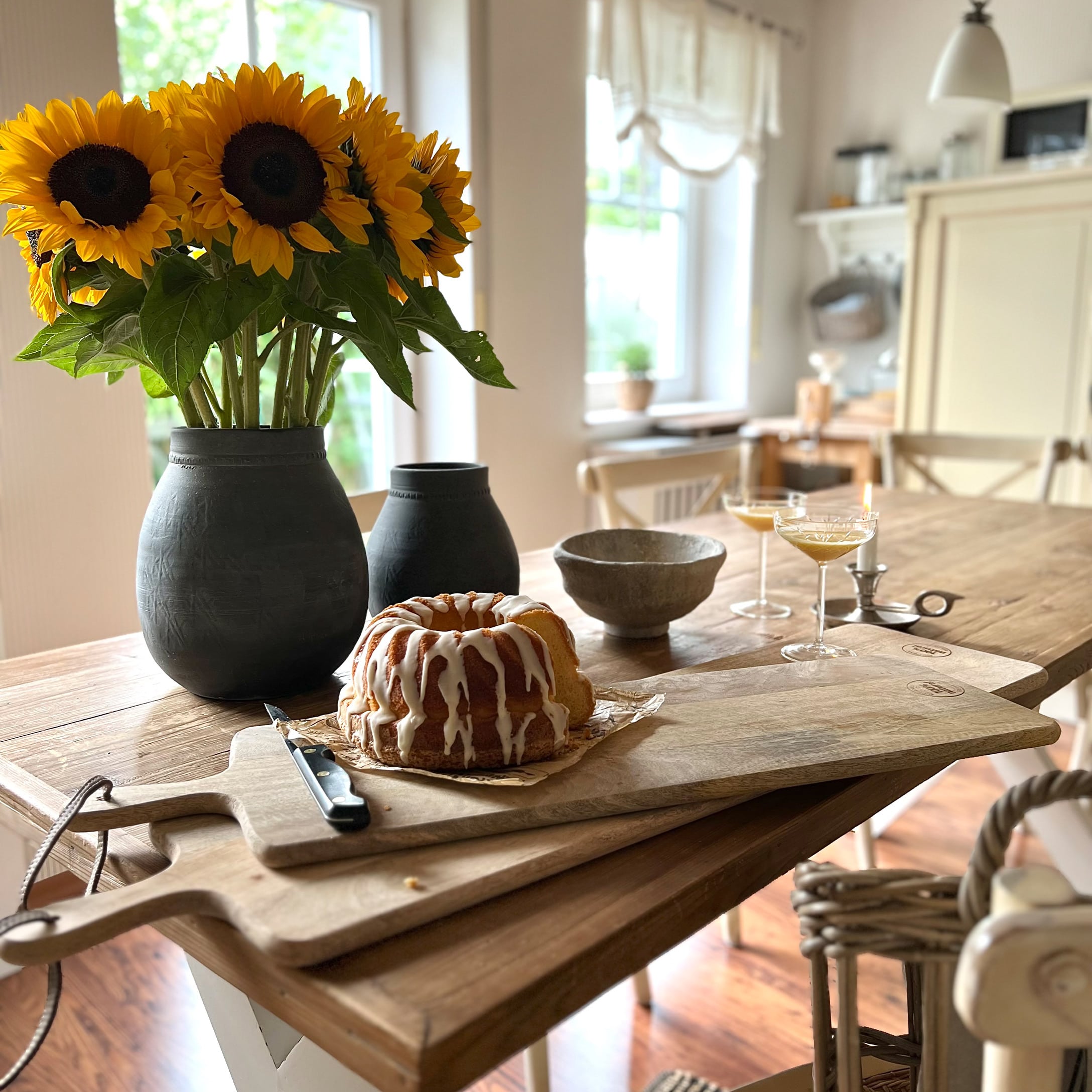 Tagliere in legno con torta e vaso nero con girasoli gialli su tavolo in legno in cucina