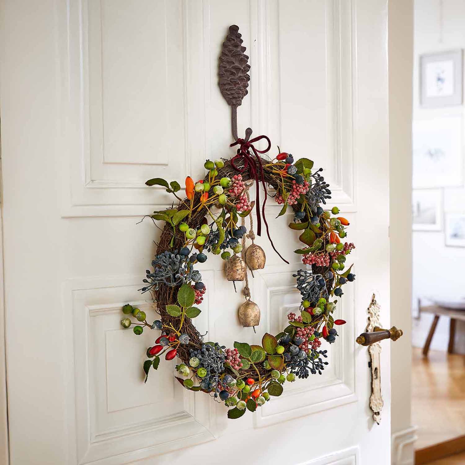 Corona decorativa con bacche colorate e campanelli appesa a porta bianca