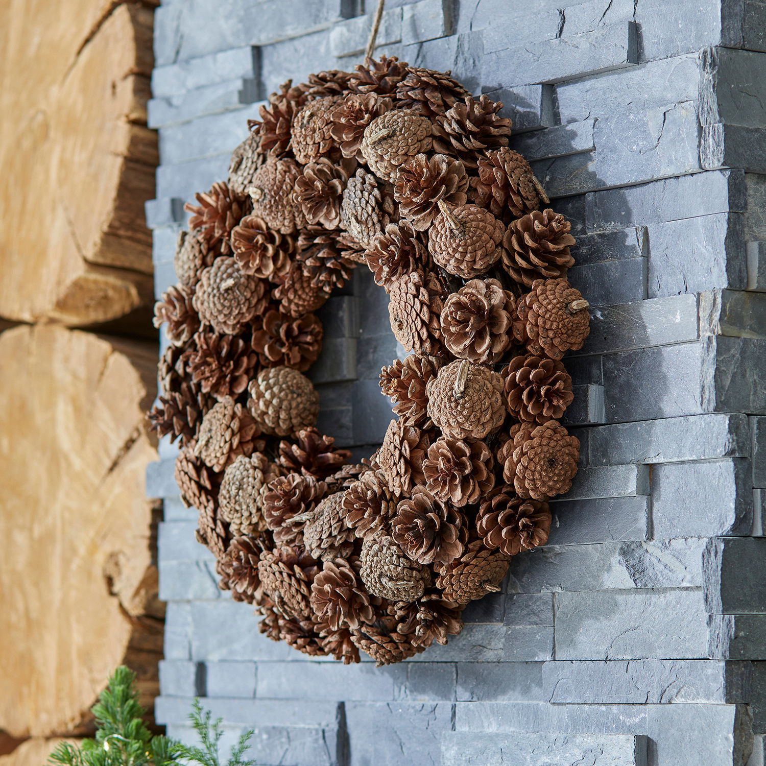 Ghirlanda Mellor Corona decorativa di pigne naturali marroni su muro di pietra grigia