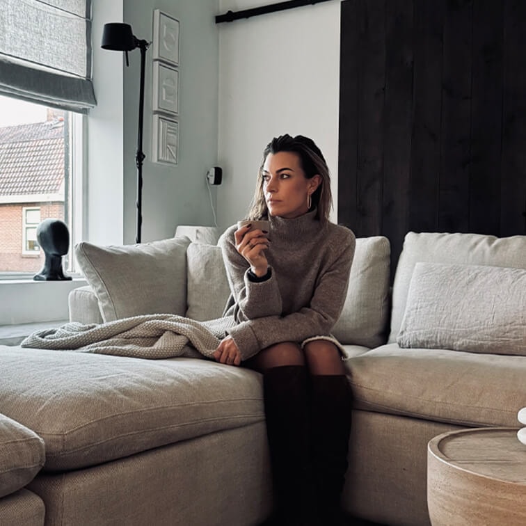 Donna con maglione grigio seduta su divano beige in soggiorno moderno con grande finestra