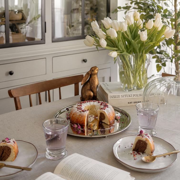 Tavolo con torta marmorizzata su vassoio d'argento, tulipani bianchi in vaso di vetro e coniglio decorativo