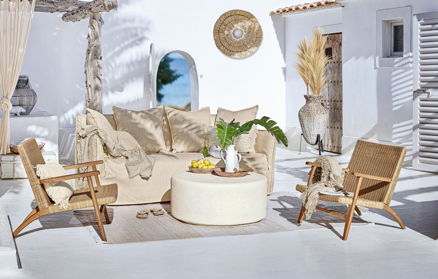 Set di mobili da giardino boho con divano beige e poltrone in rattan su terrazza soleggiata
