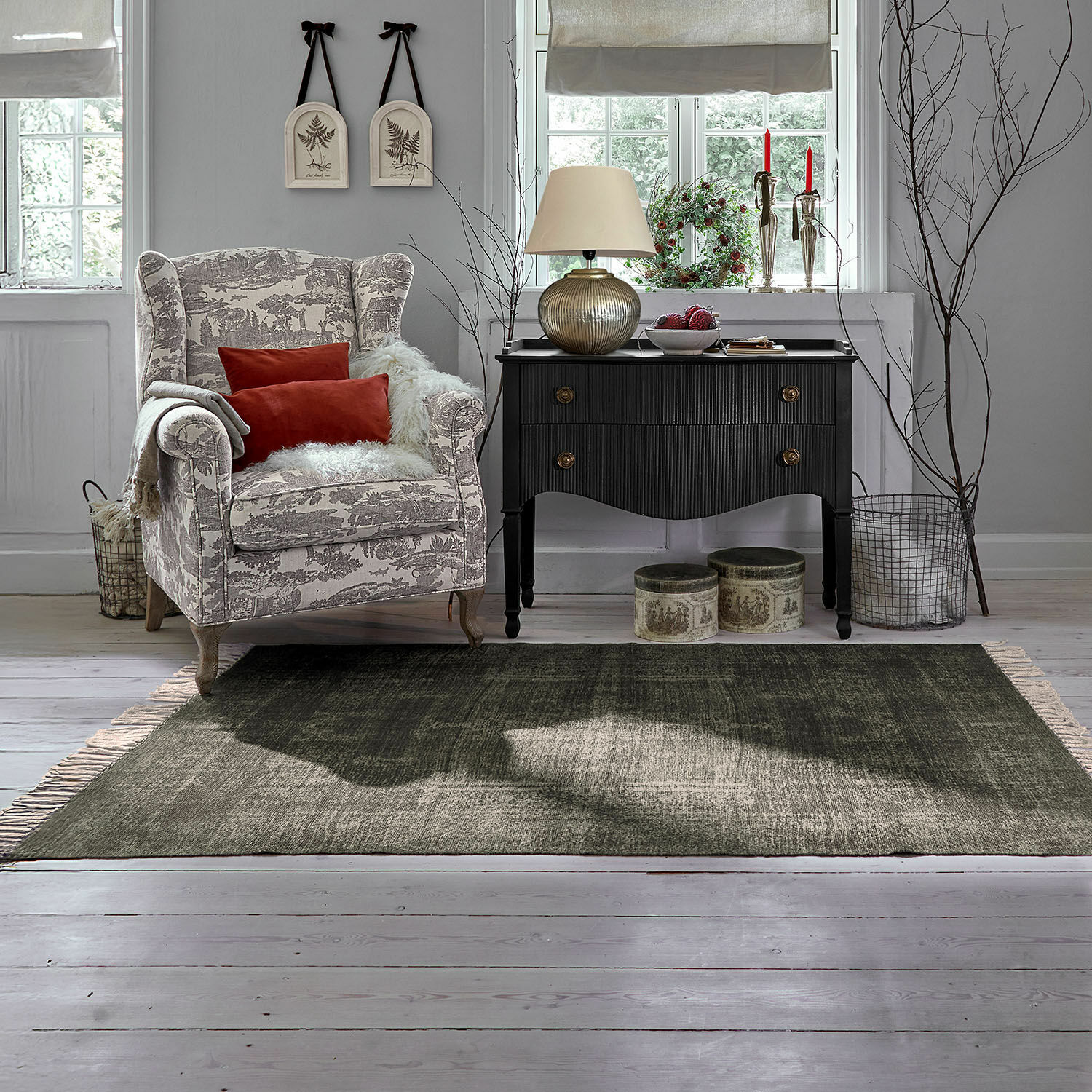 Poltrona accogliente beige con motivo grigio e cuscini rossi accanto a comò nero vintage in soggiorno