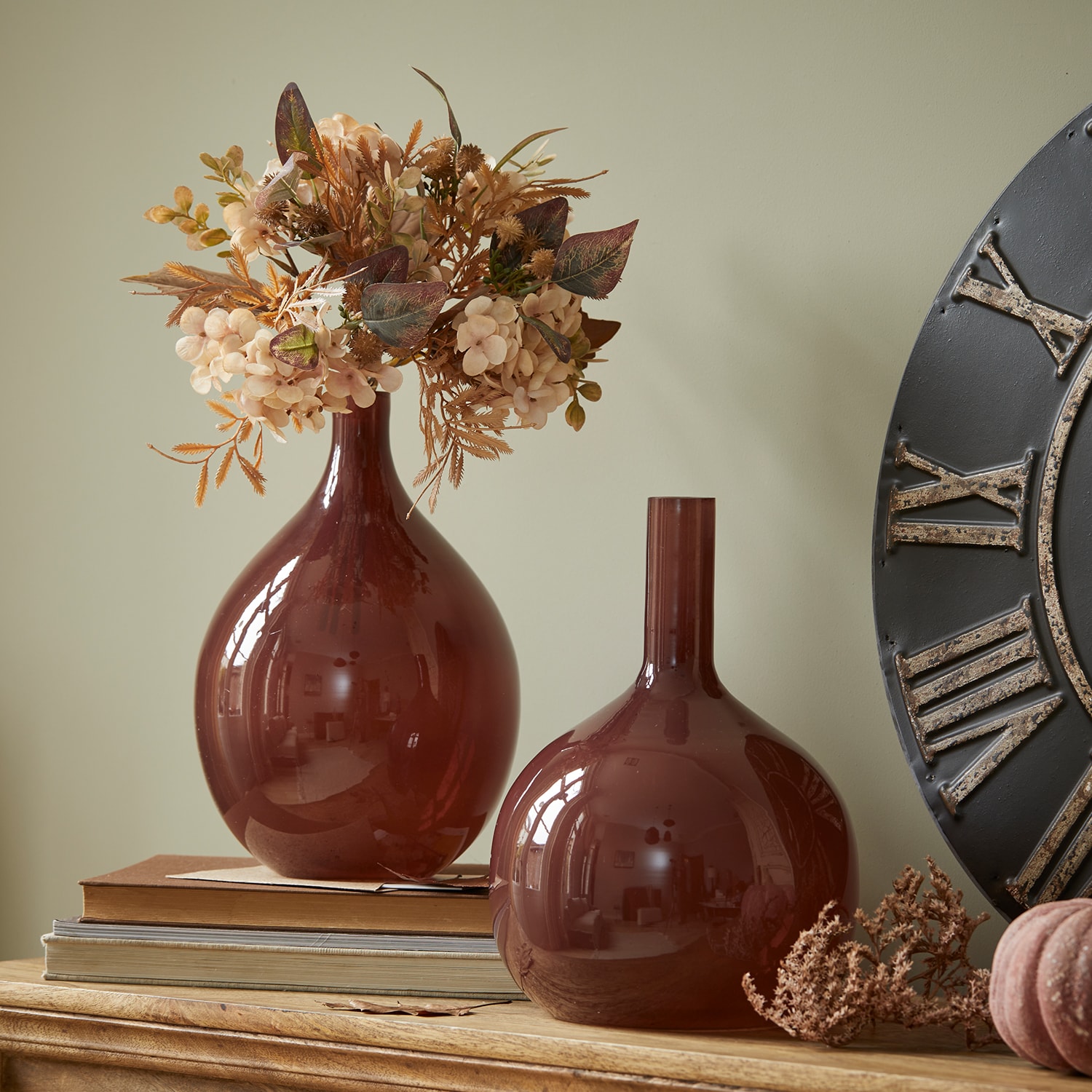 Due vasi decorativi in vetro bordeaux su tavolo in legno con fiori secchi e libri