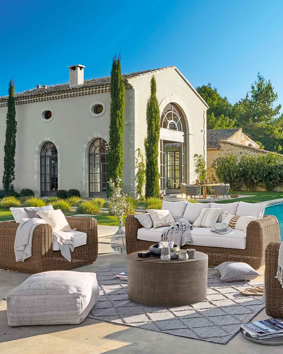 Set di mobili da giardino in rattan marrone con cuscini bianchi su terrazza vicino piscina soleggiata
