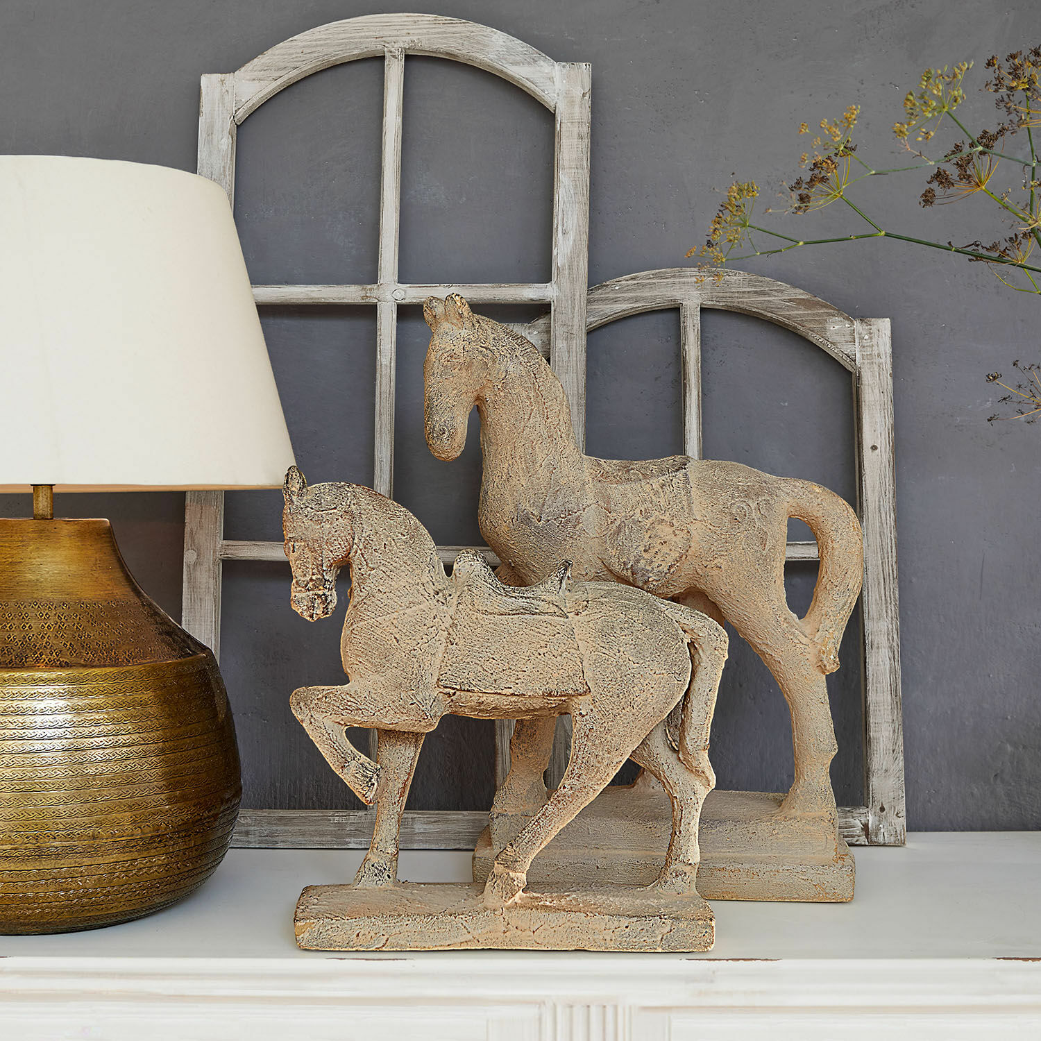 Coppia di cavalli decorativi Mirandel Figure decorative di cavalli in pietra beige su mensola bianca con lampada e cornici di finestre in legno