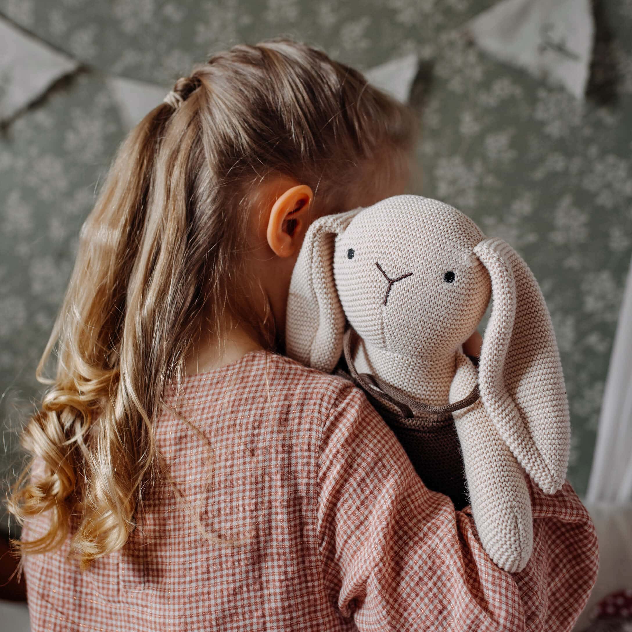 Bambina abbraccia coniglio di peluche beige lavorato a maglia in camera dei bambini