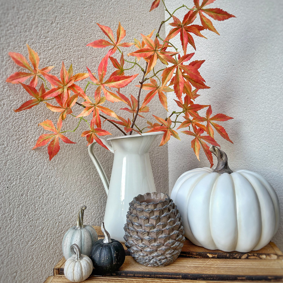 Brocca bianca decorativa con foglie arancioni-rosse e zucche decorative su mensola in legno