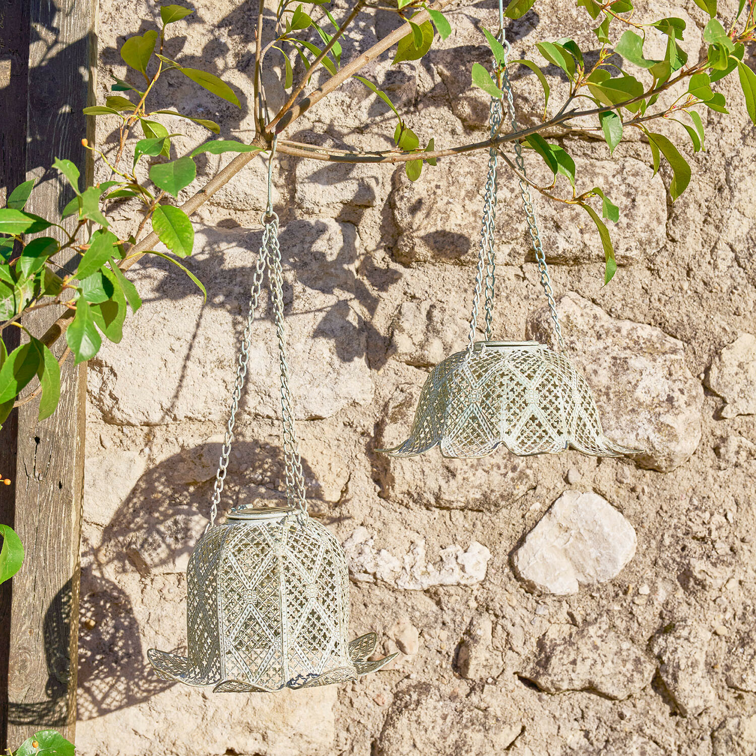 Due lanterne sospese in metallo grigio chiaro a forma di campana davanti a un muro di pietra