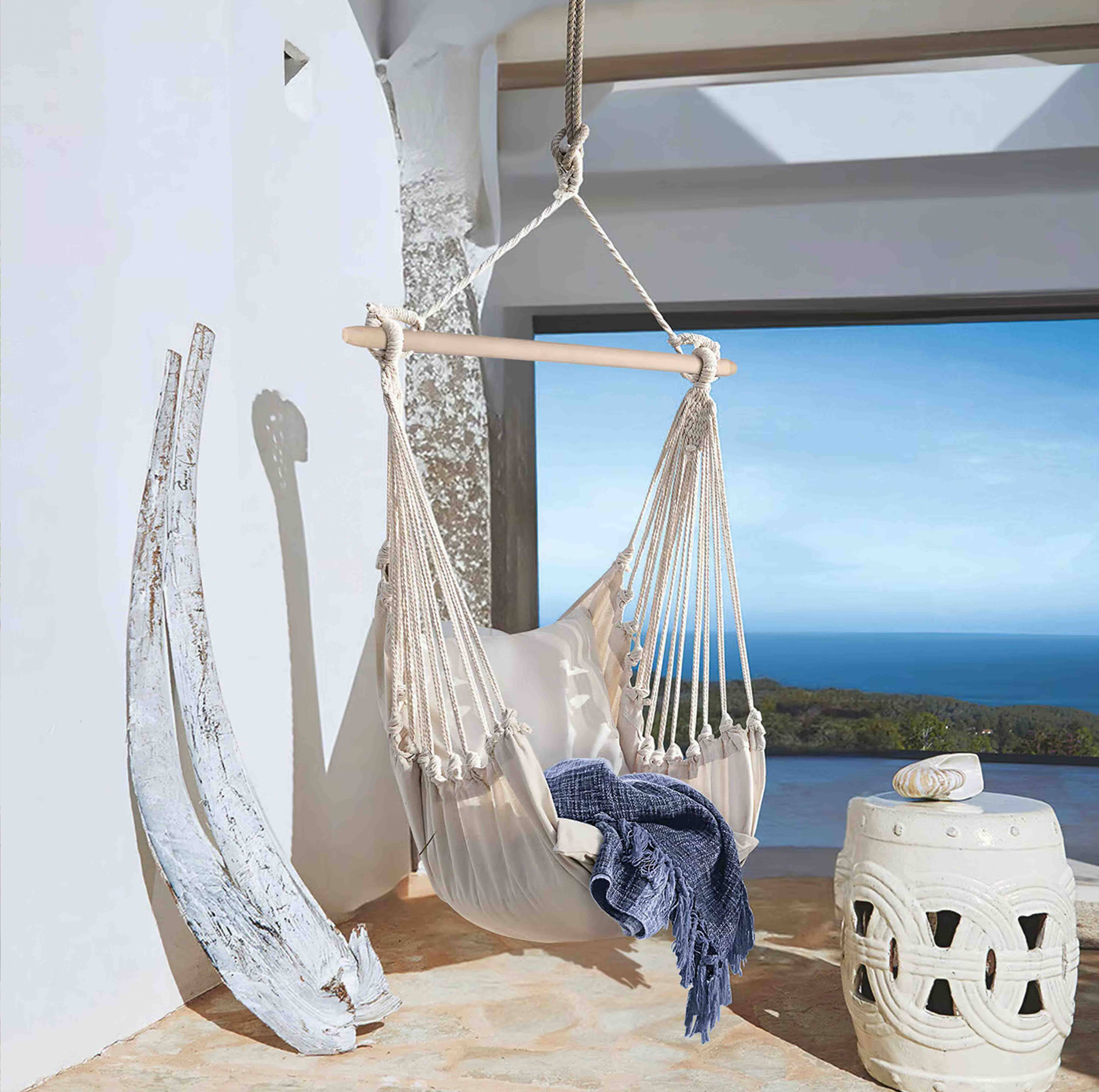Amaca beige in cotone con barra in legno e coperta blu su terrazza con vista mare