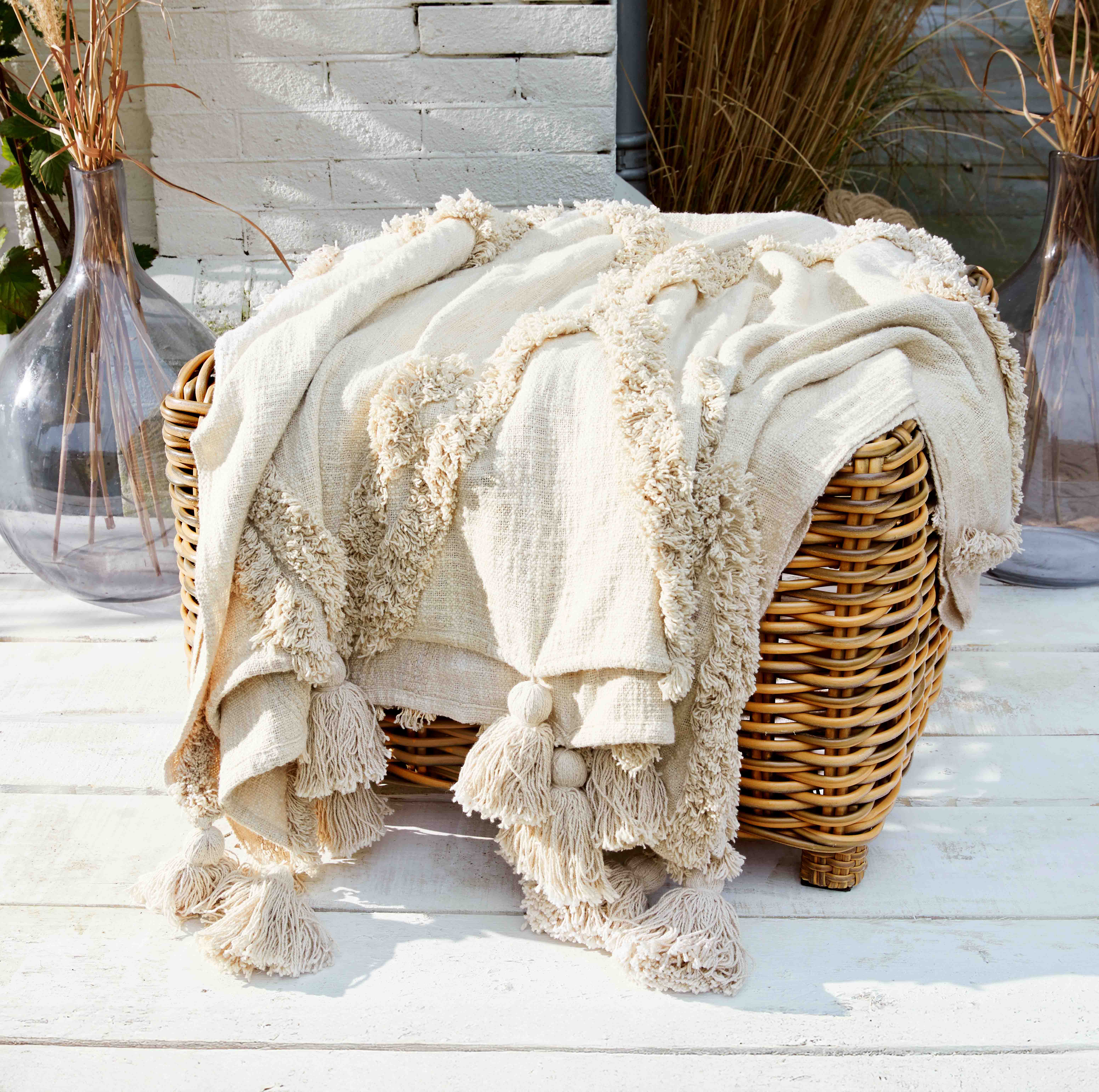 Coperta crema con frange in tessuto morbido su poltrona in vimini, decorazione per interni e giardino