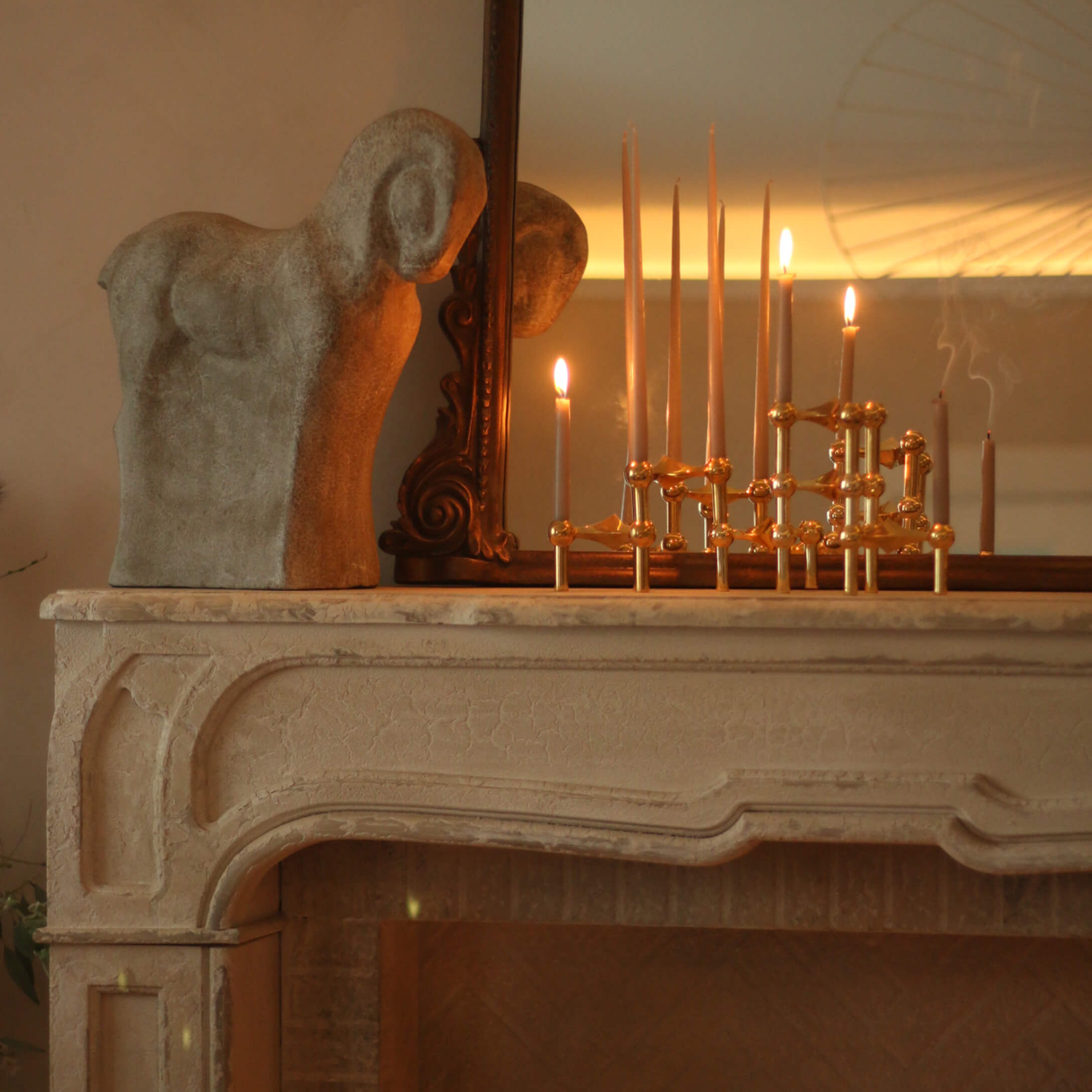 Scultura decorativa di ariete in pietra su camino con candelabro in ottone e candele accese