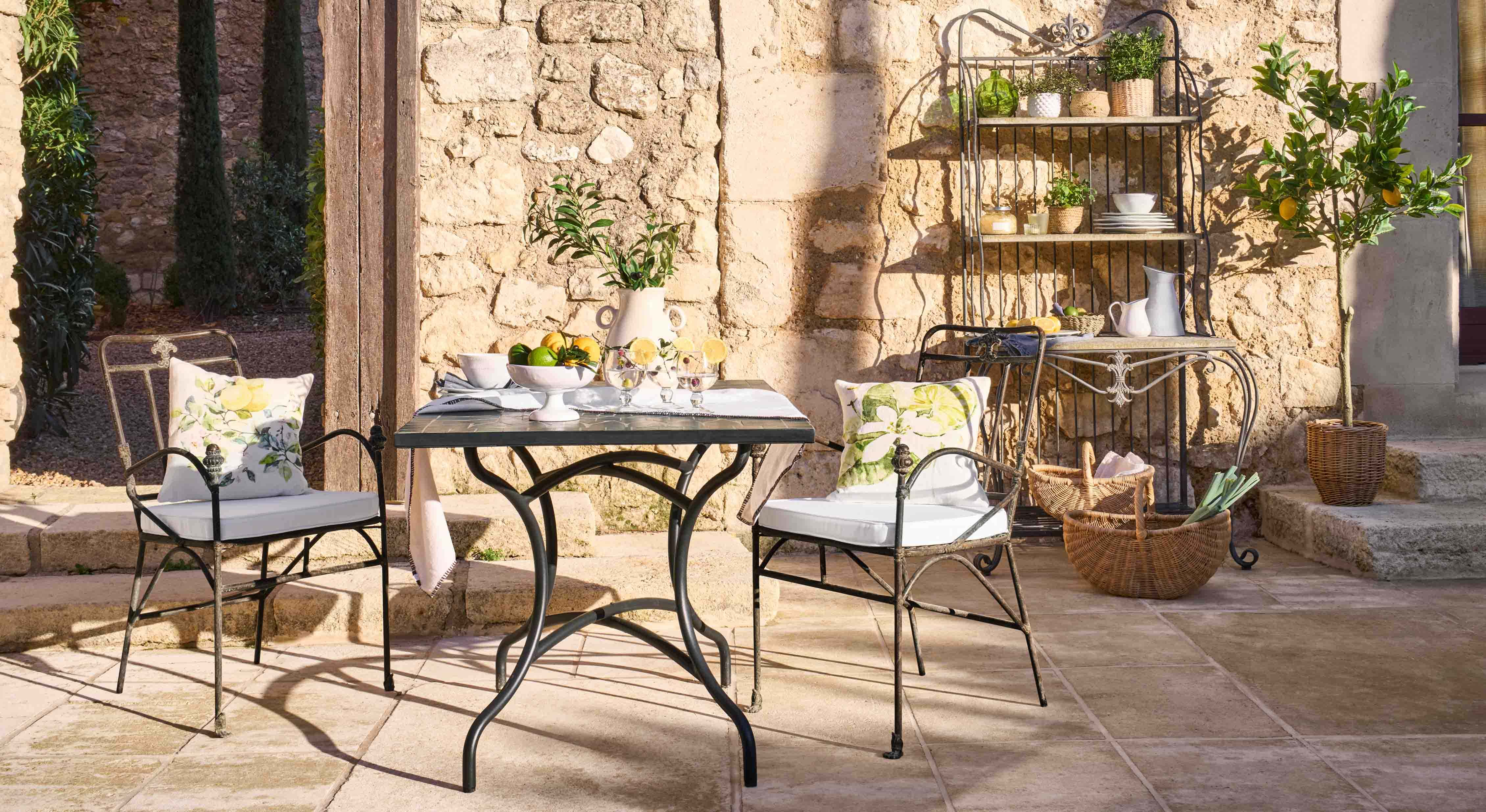 Tavolo e sedie in metallo con cuscini floreali su patio in pietra con decorazioni da giardino