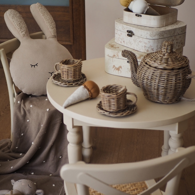 Set da tè in vimini su tavolo bianco con cuscino coniglio di peluche e coperta marrone