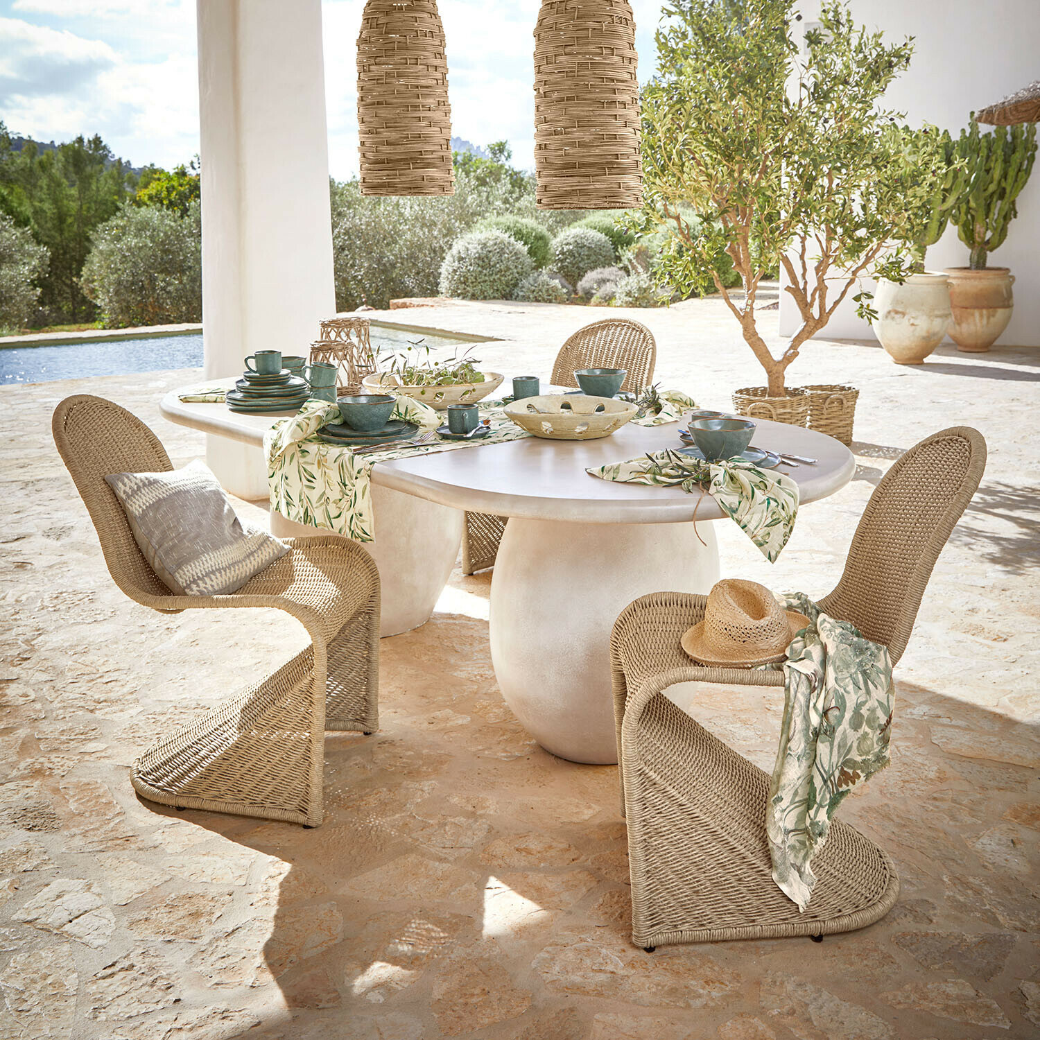 Tavolo Arevalon Tavolo ovale con piano bianco e sedie in vimini naturale su terrazza con vista giardino