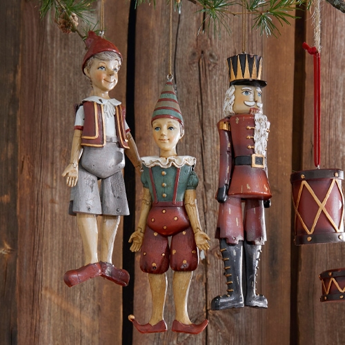 Tre decorazioni natalizie in legno vintage rosse e verdi appese davanti a una parete di legno rustica
