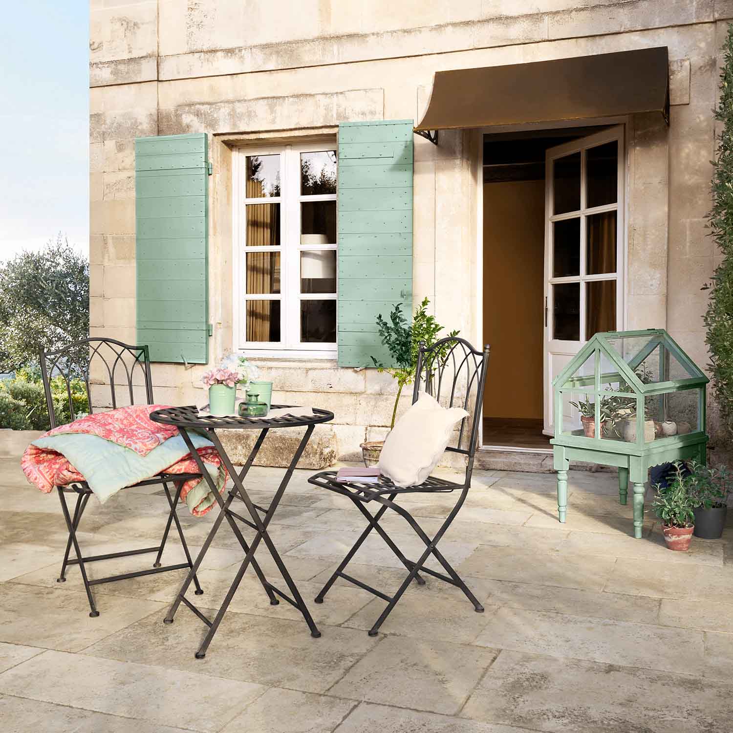 Set da giardino in metallo con tavolo e sedie su terrazza, mini serra verde e accessori pastello