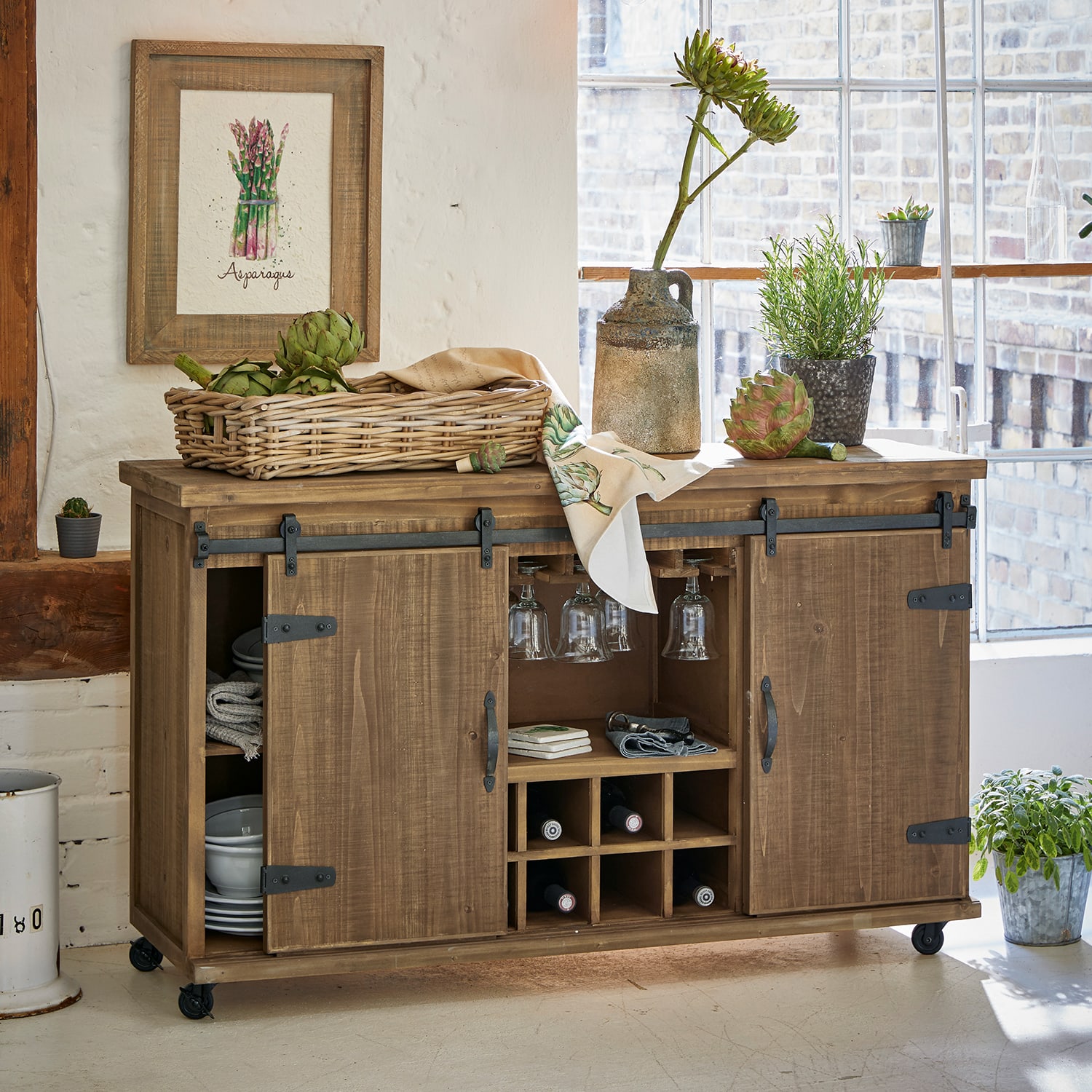 Credenza in legno su ruote con portabottiglie e porta bicchieri, decorata con piante e cesta di verdure