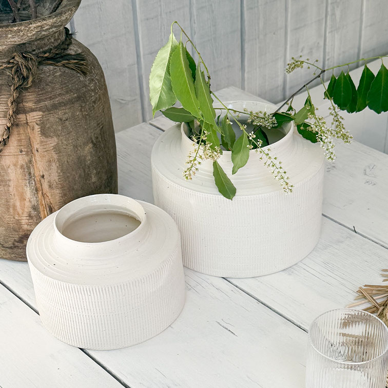 Vasi in ceramica bianca opaca su tavolo in legno con foglie verdi e fiori bianchi