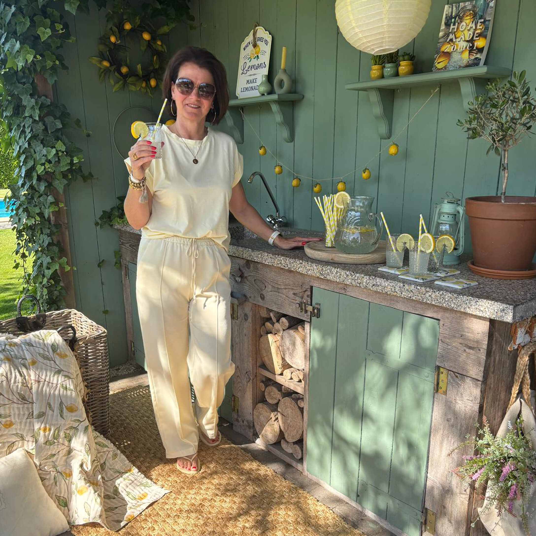Donna con abito crema vicino a cucina esterna verde con limonata e decorazioni di limoni