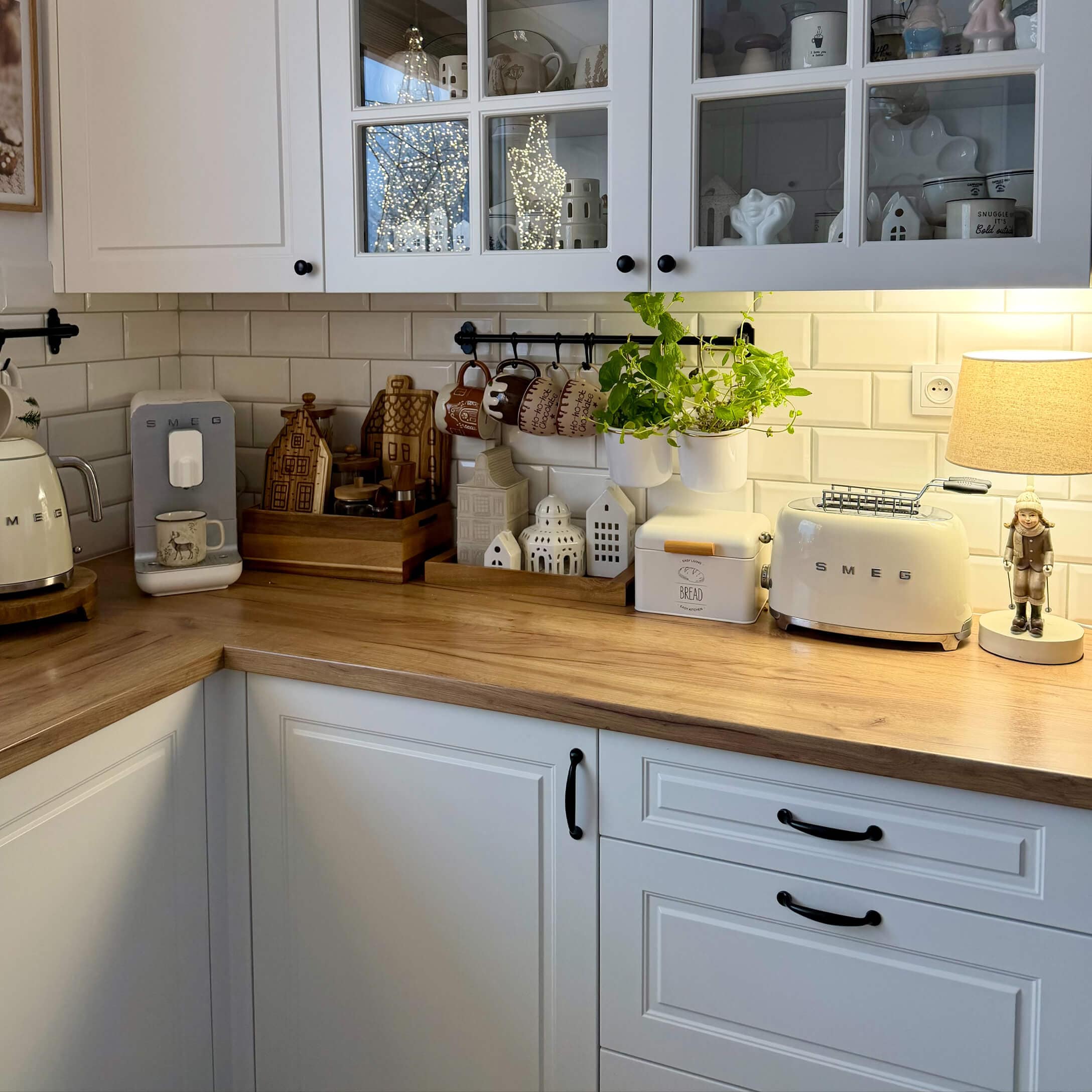 Cucina con mobili bianchi, piano in legno, elettrodomestici SMEG crema e decorazioni con piante verdi