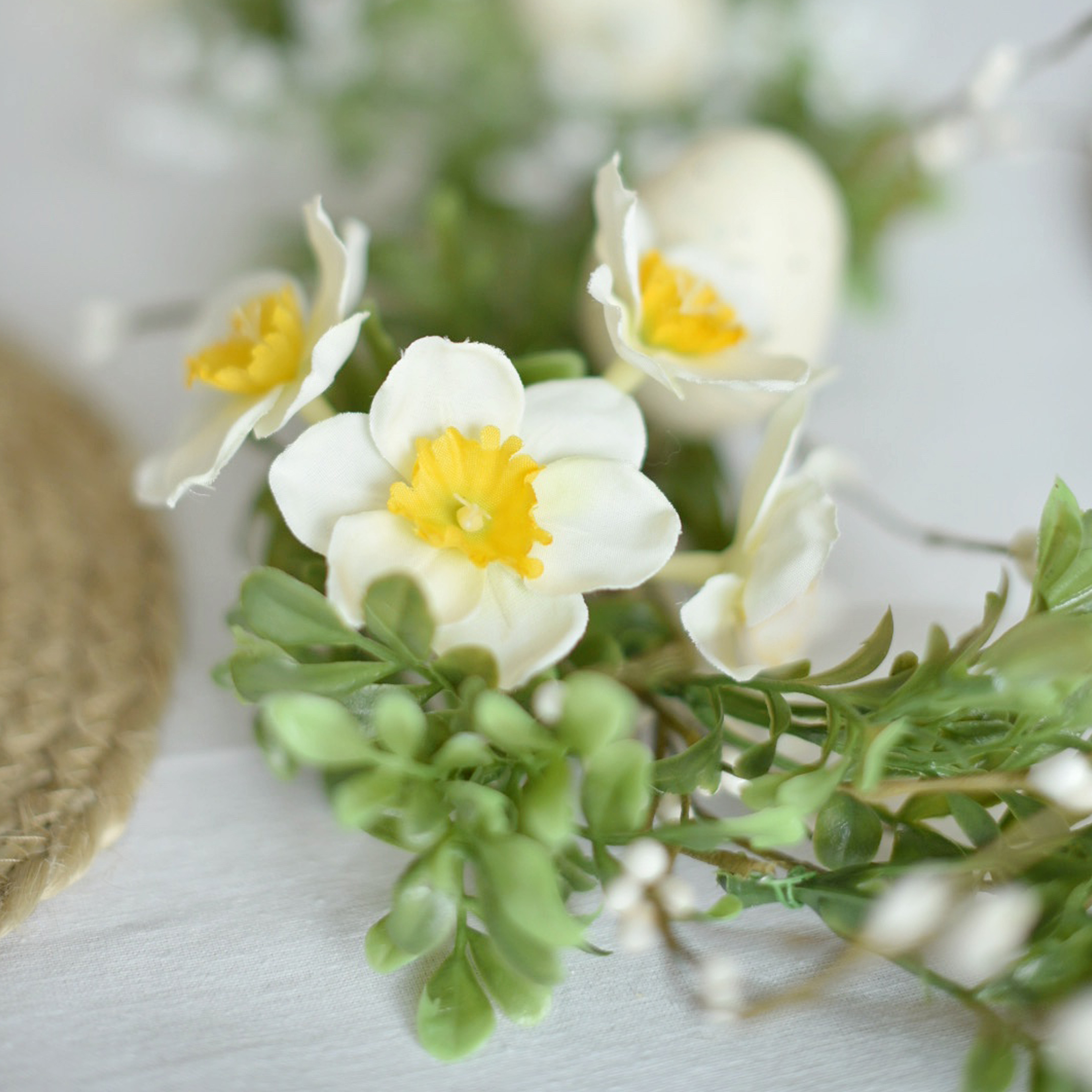 Corona decorativa con fiori bianchi e gialli e foglie verdi su sfondo chiaro