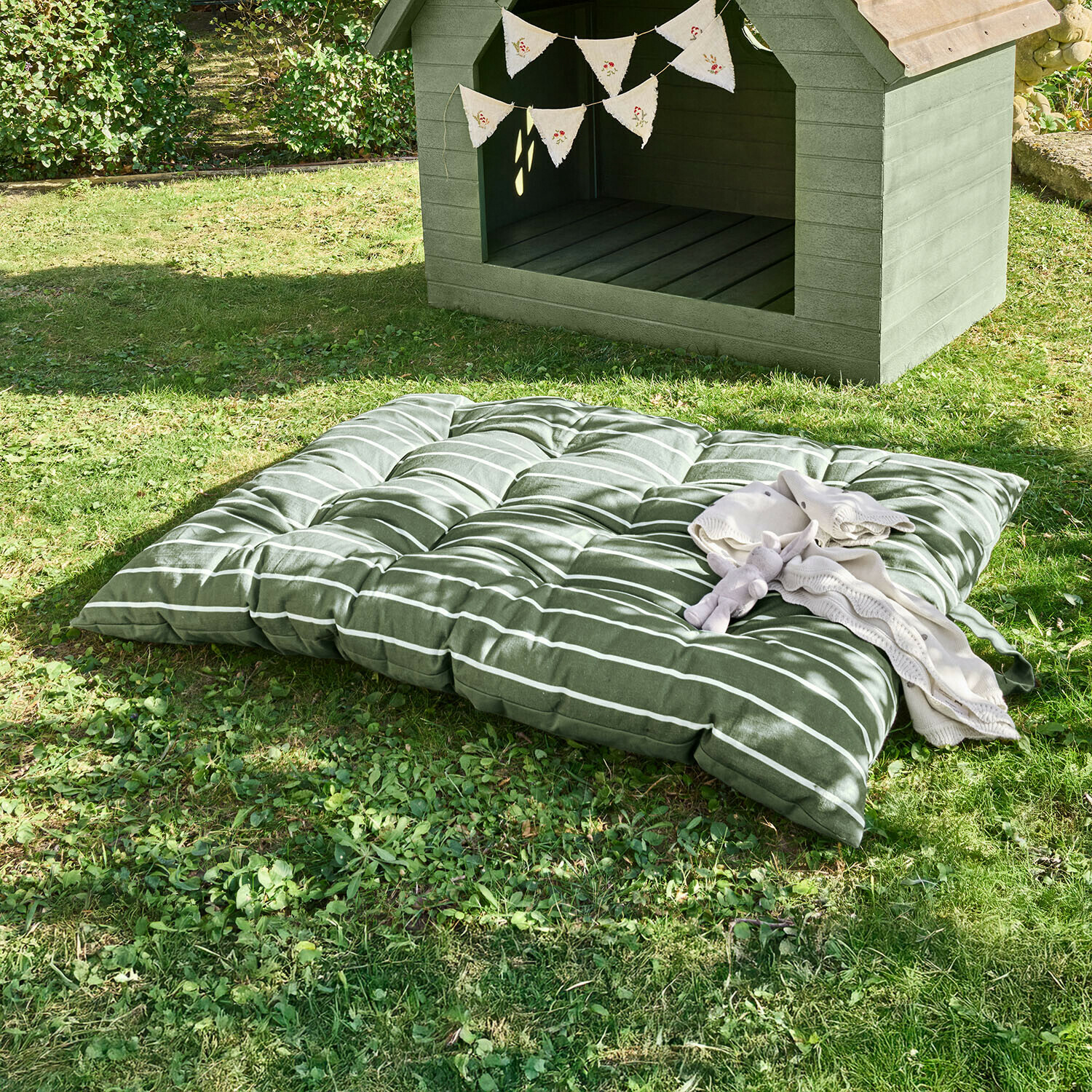 Morbido cuscino verde a righe sull'erba accanto a una cuccia in legno con ghirlanda decorativa