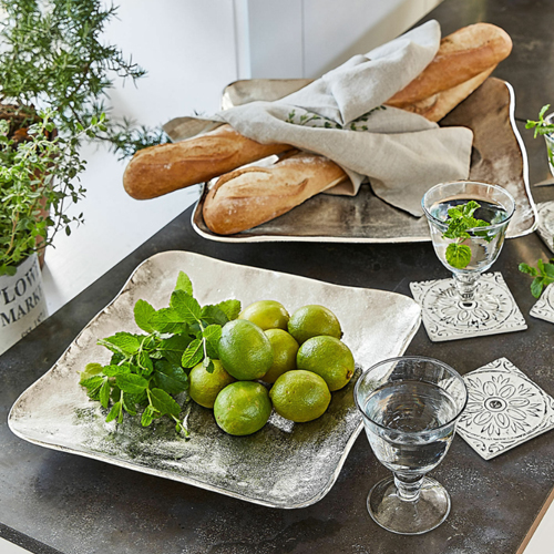 Vassoio quadrato in metallo argentato con lime e menta su tavolo con baguette e bicchieri d'acqua