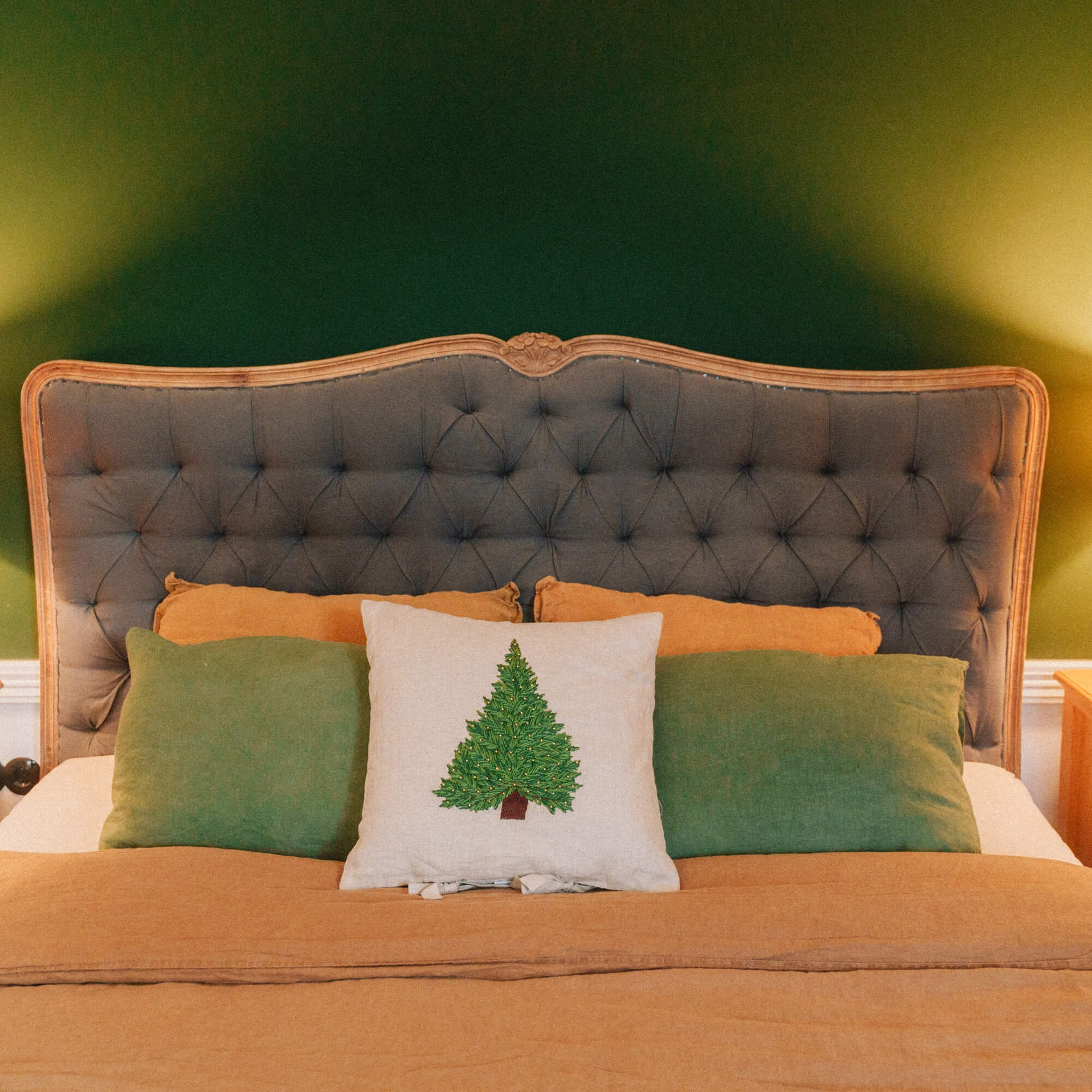 Camera da letto con testiera imbottita grigia e cuscino con albero di Natale su biancheria da letto arancione