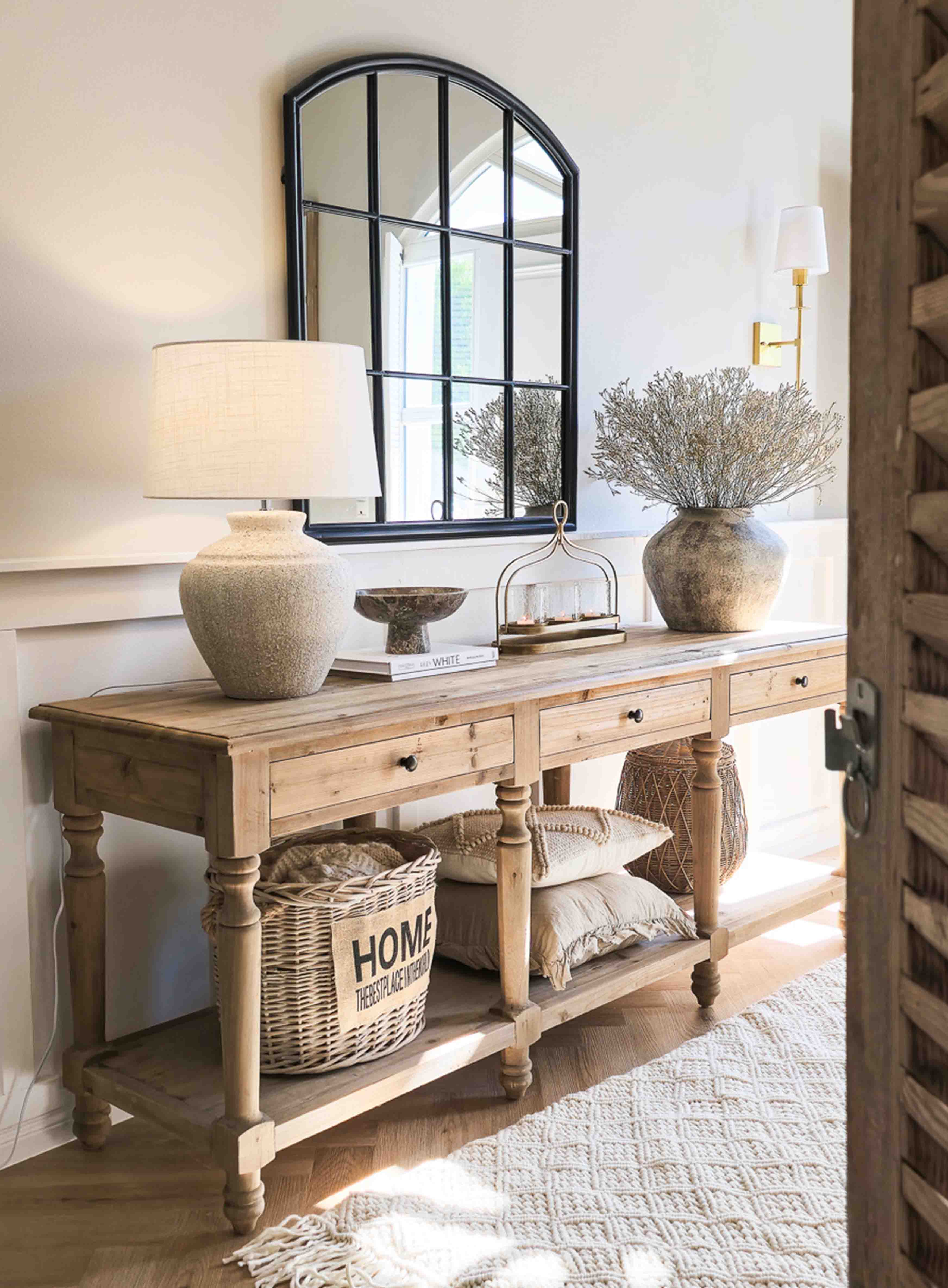 Consolle in legno con lampada in ceramica, specchio con cornice nera e decorazioni rustiche in ambiente luminoso