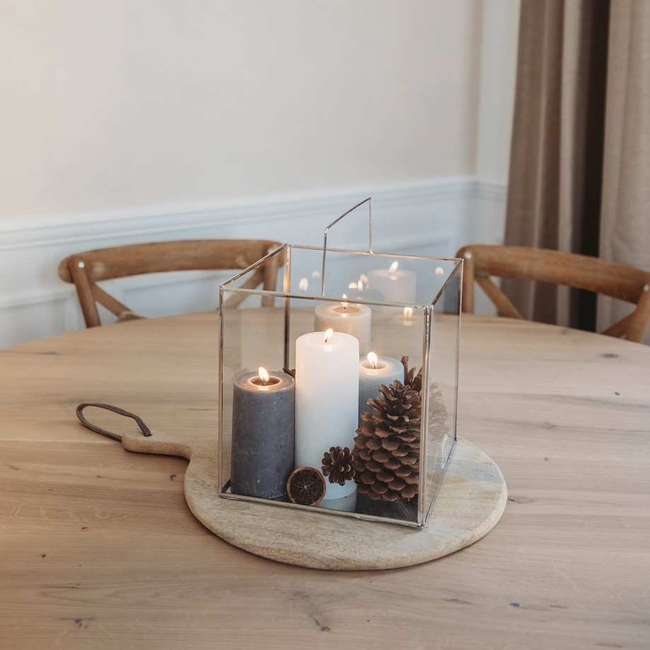 Lanterna in vetro con tre candele e pigne su tagliere in legno, decorazione natalizia sul tavolo