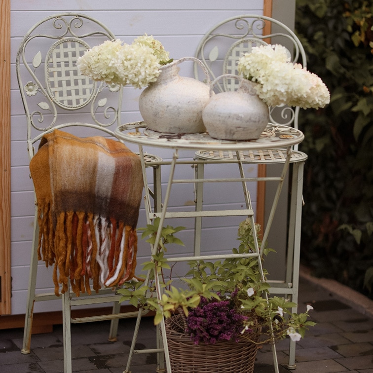 Tavolo e due sedie vintage in metallo chiaro con vasi decorativi e fiori bianchi