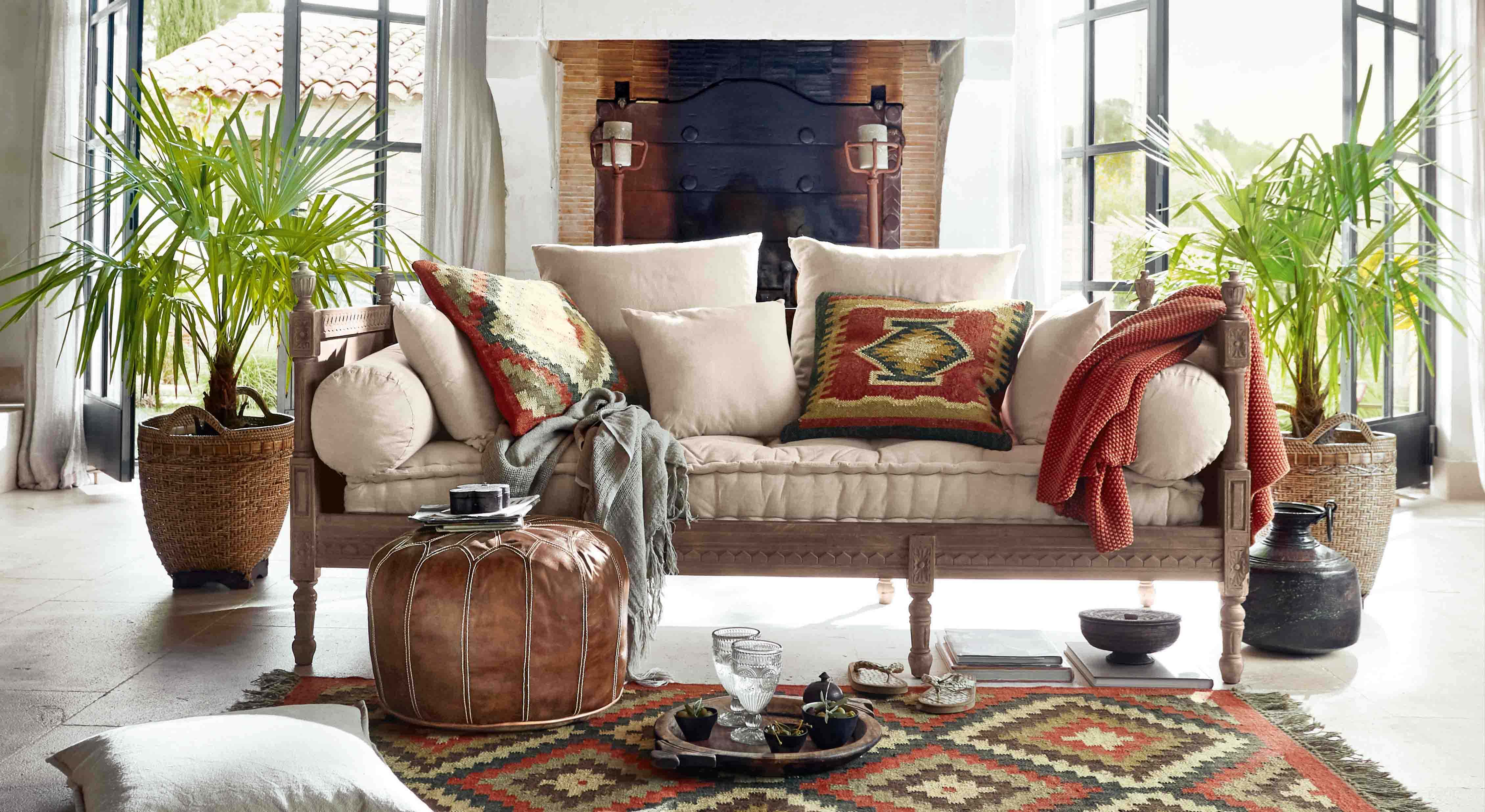 Divano con rivestimento beige chiaro e struttura in legno, cuscini colorati e coperta in stile boho in soggiorno luminoso