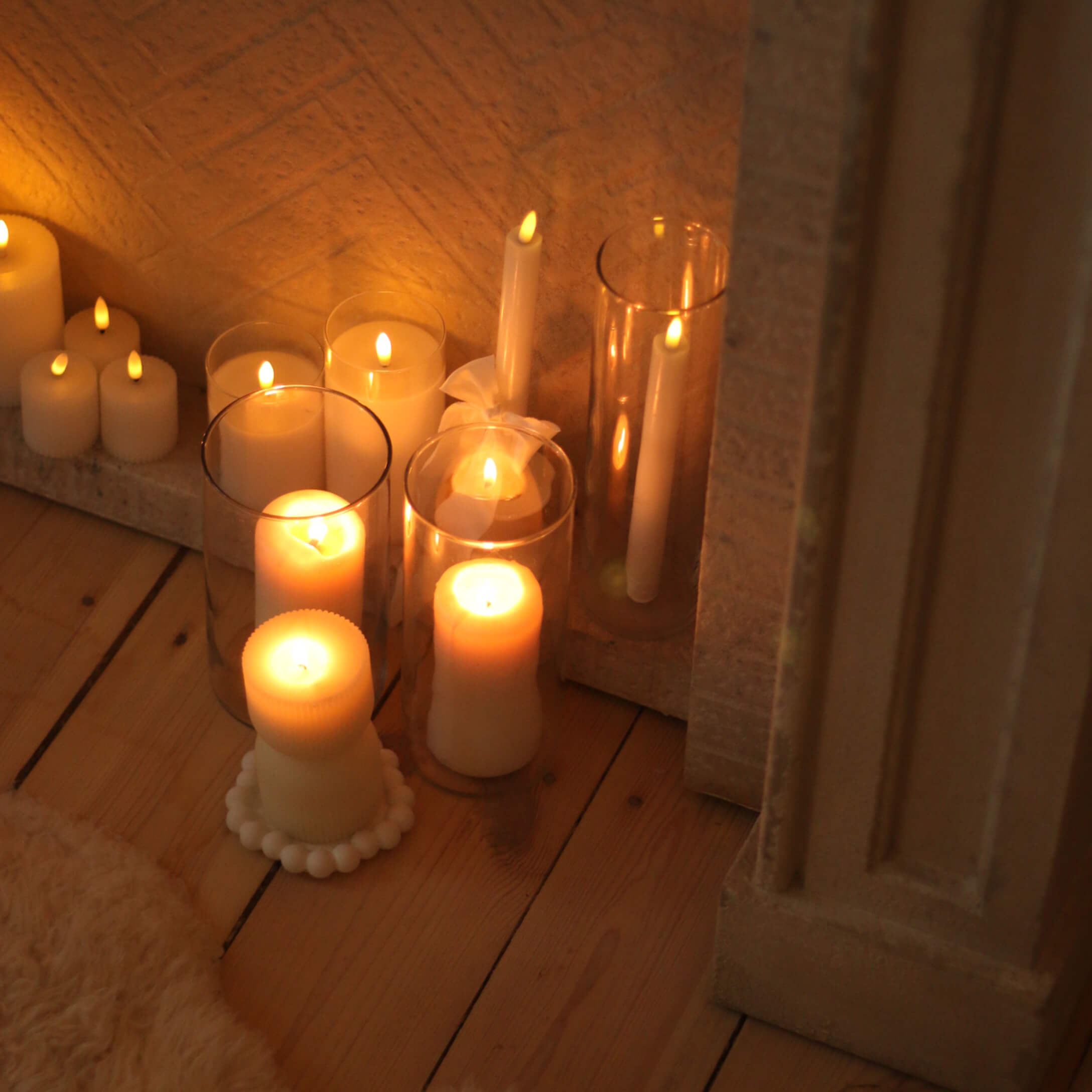 Set di candele bianche di varie forme e dimensioni su pavimento in legno, decorazione d'interni