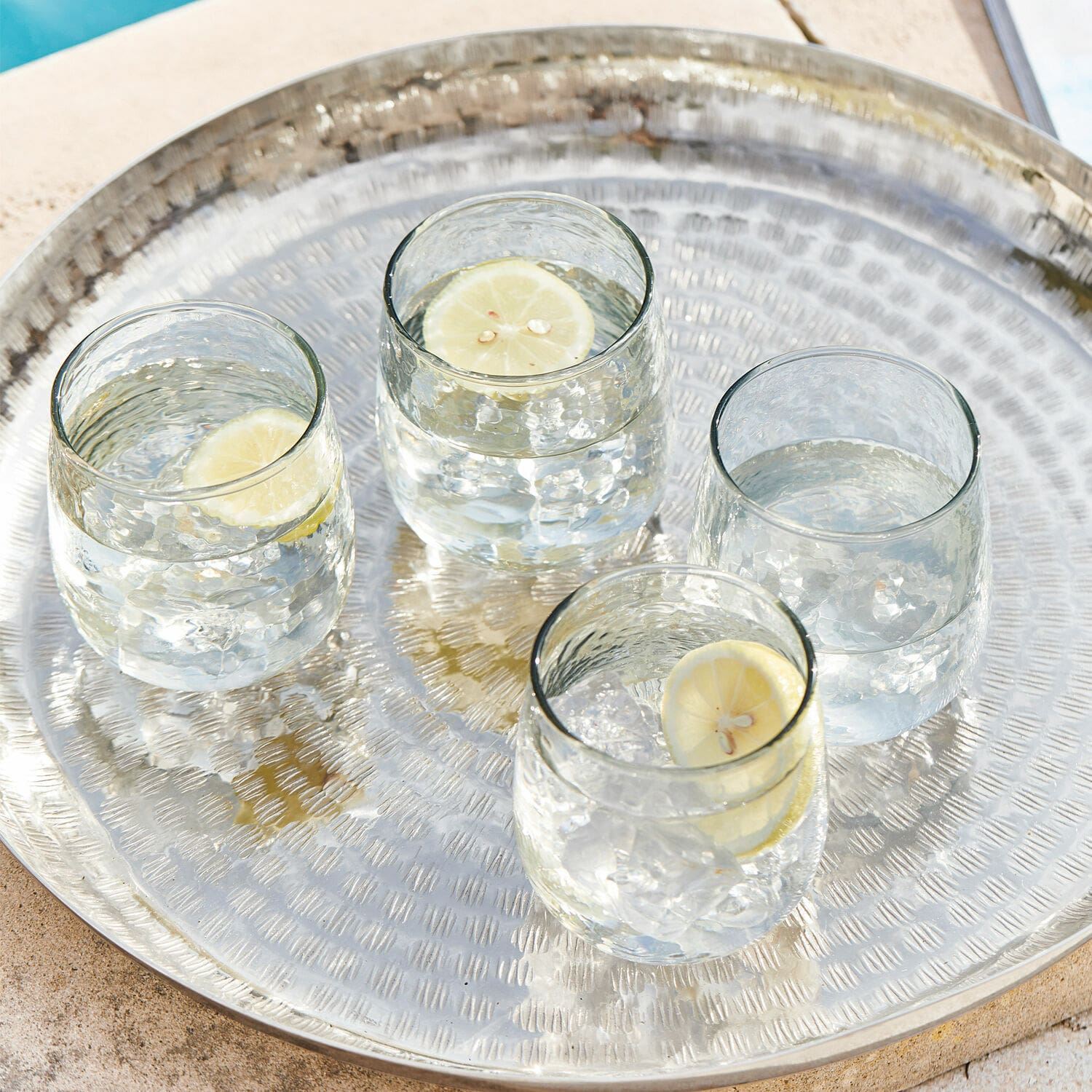 Set di 4 bicchieri Valters Vassoio in metallo con quattro bicchieri d'acqua e fette di limone vicino alla piscina