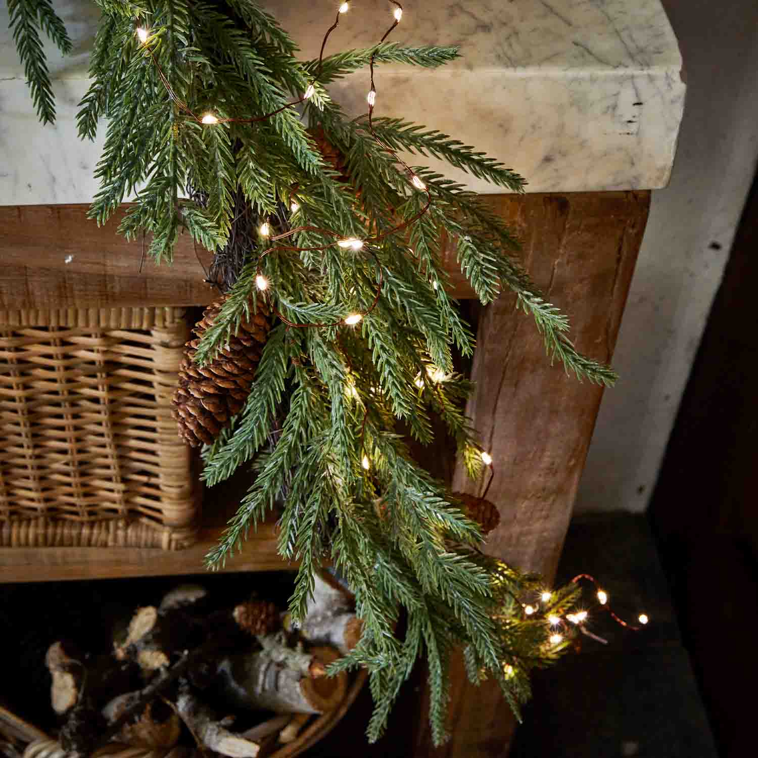 Ramo di abete con pigna e luci LED su camino in legno, decorazione natalizia