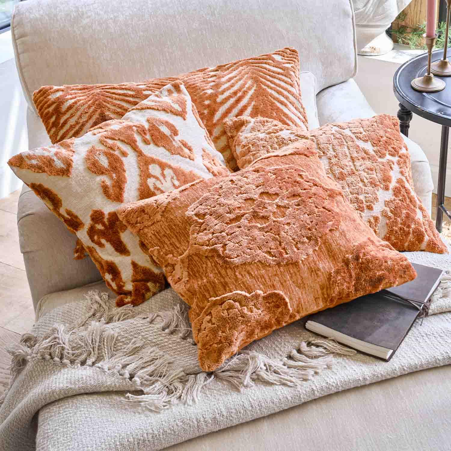 Set di cuscini decorativi arancioni con motivi su divano chiaro con coperta a frange