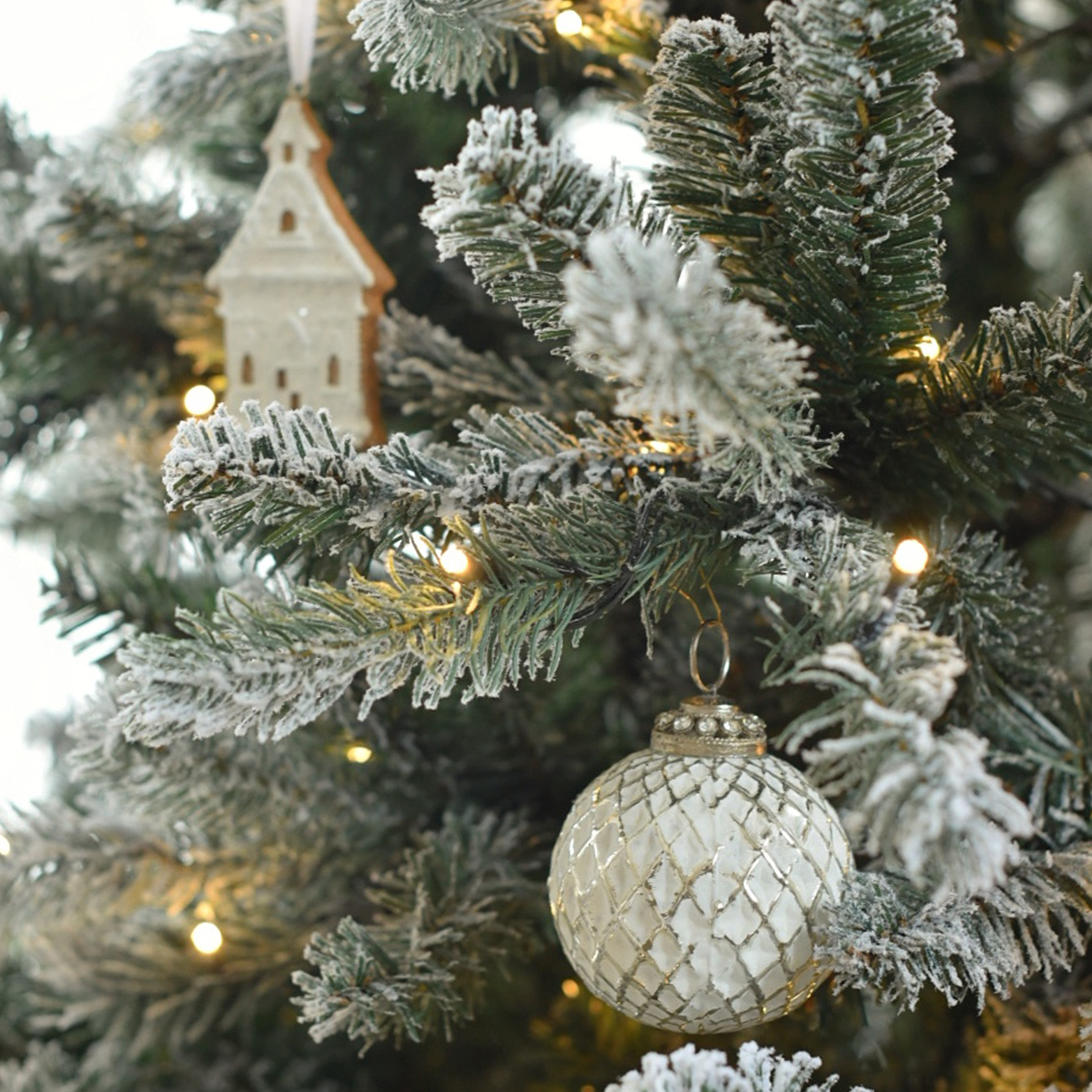 Pallina di Natale in vetro bianco con motivo a griglia su albero innevato con luci LED e decorazione in legno