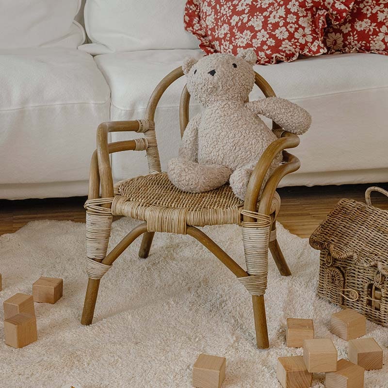 Sedia per bambini in rattan con orsetto di peluche beige su tappeto chiaro e blocchi di legno